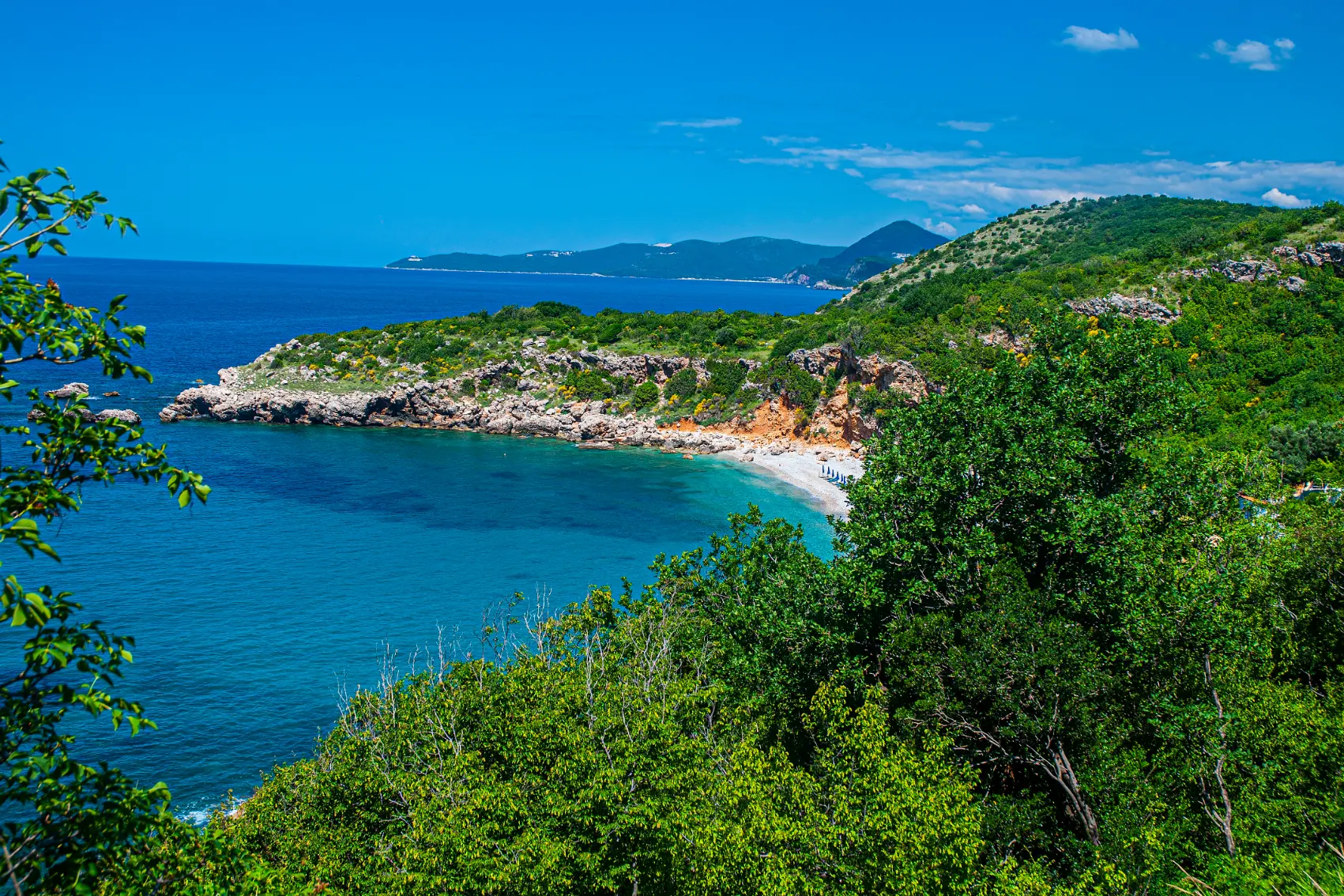 Elevated view of Drobni Pijesak Beach through dense forest on a sunny day in Montenegro