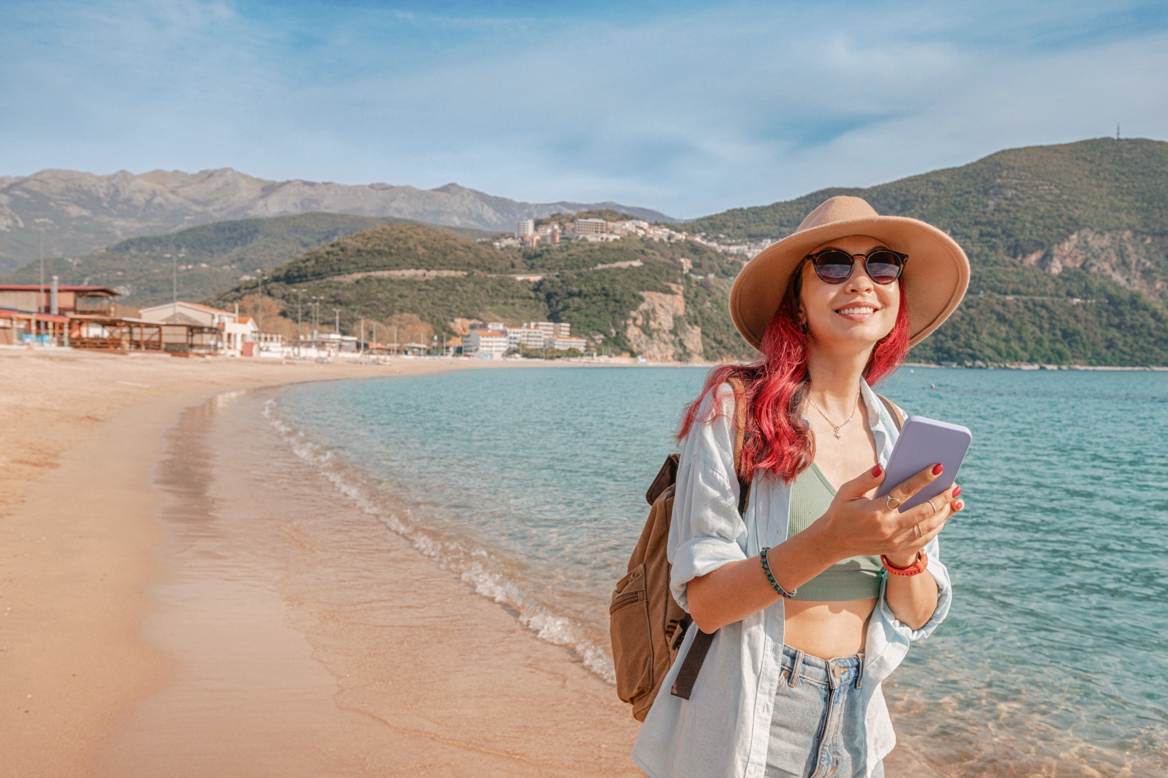 A woman traveller walks along Jaz Beach with her phone
