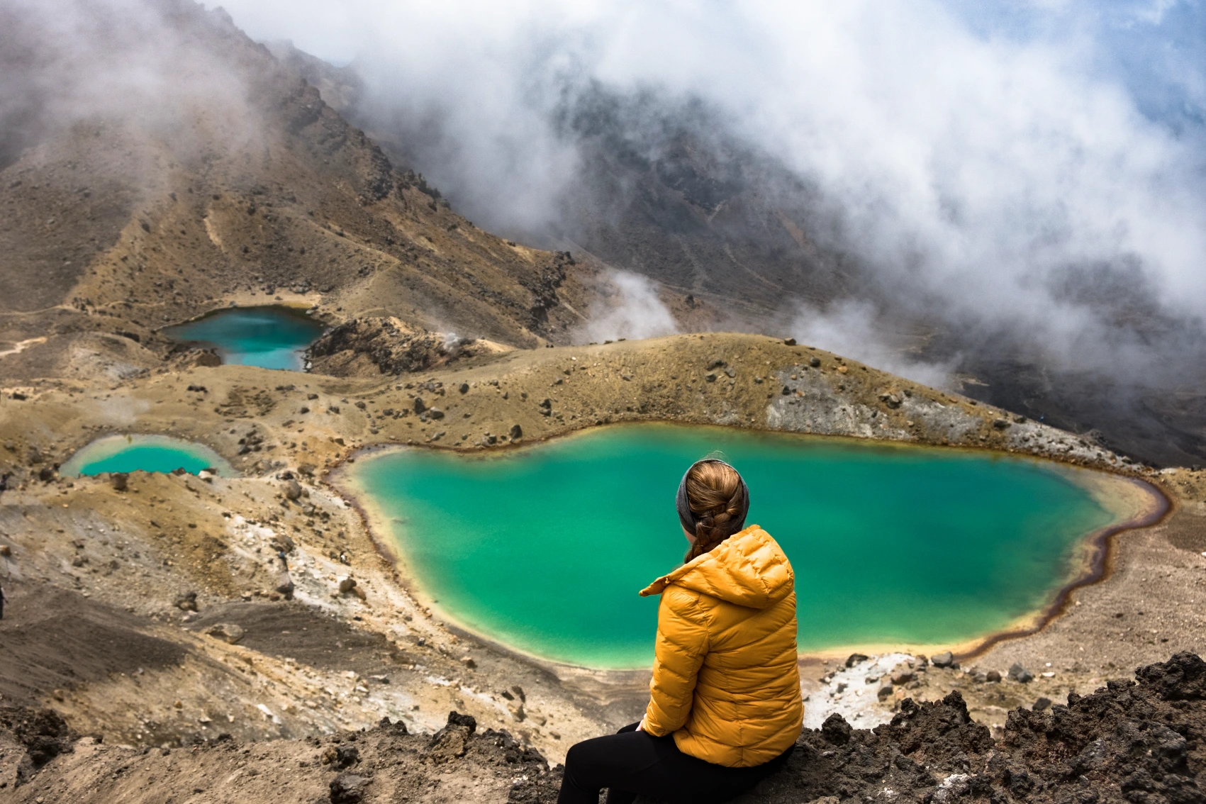 Tongariro Alpine Crossing, New Zealand A hiker sits in front of a colourful lake on the Tongariro Alpine Crossing hike in New Zealand