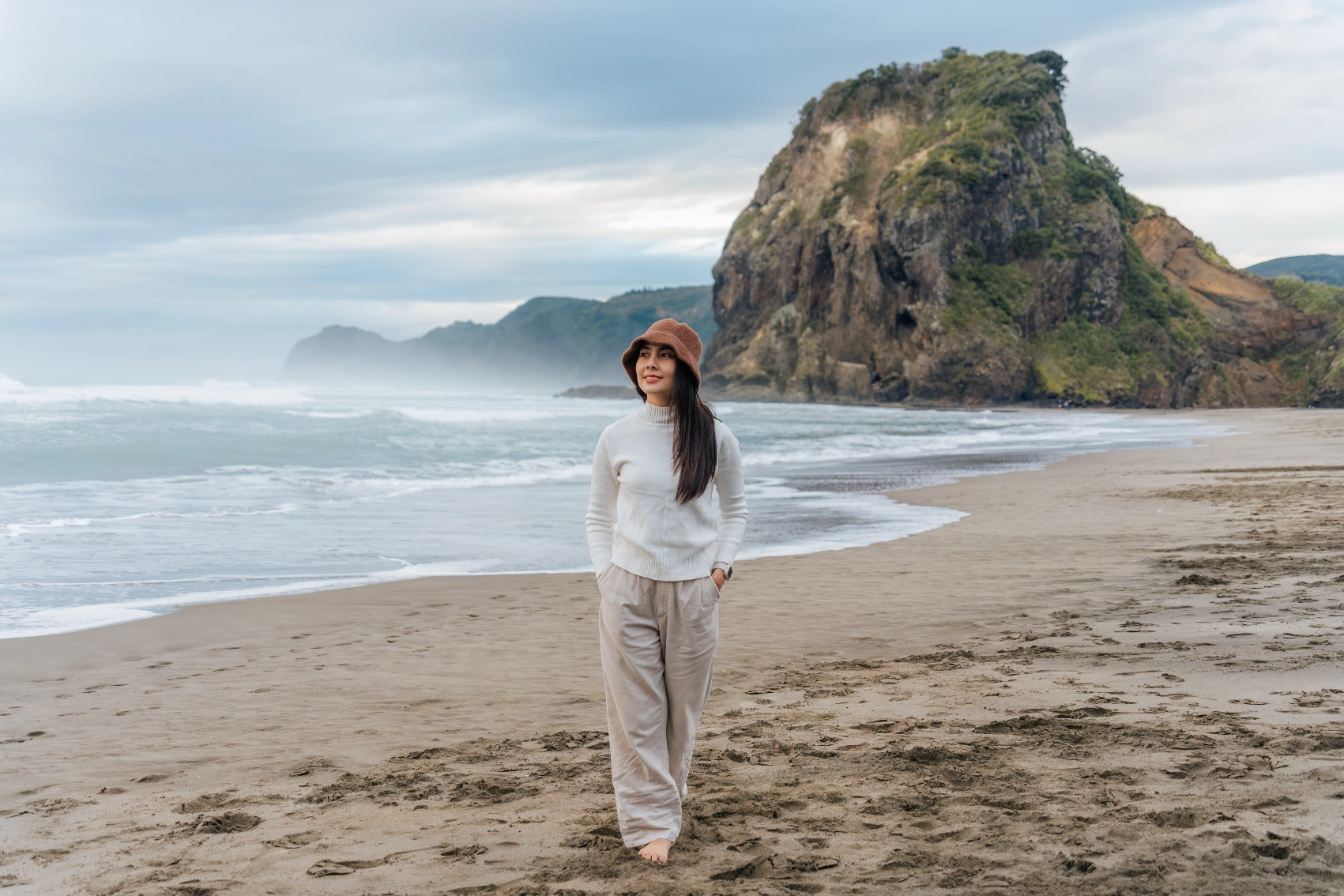 A woman walks on Piha Beach in New Zealand