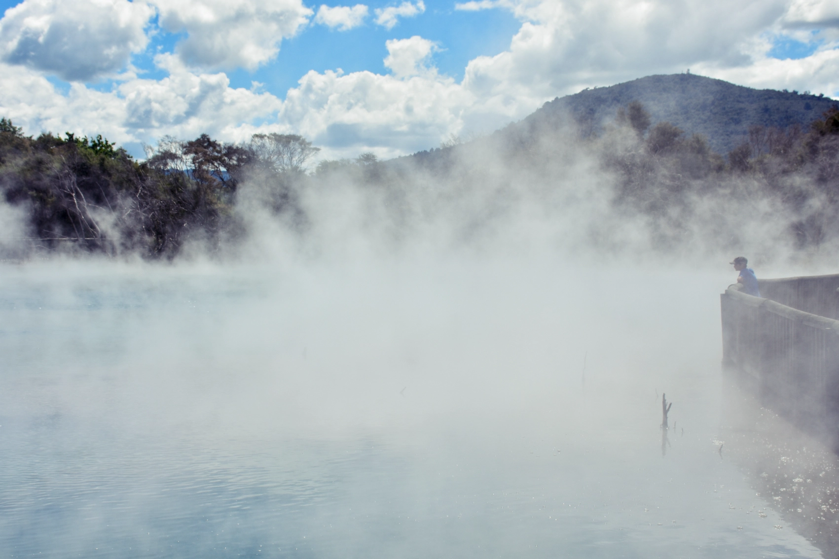 A traveller stands on a platform surrounded by vapour at a geothermal pool in Rotorua, New Zealand