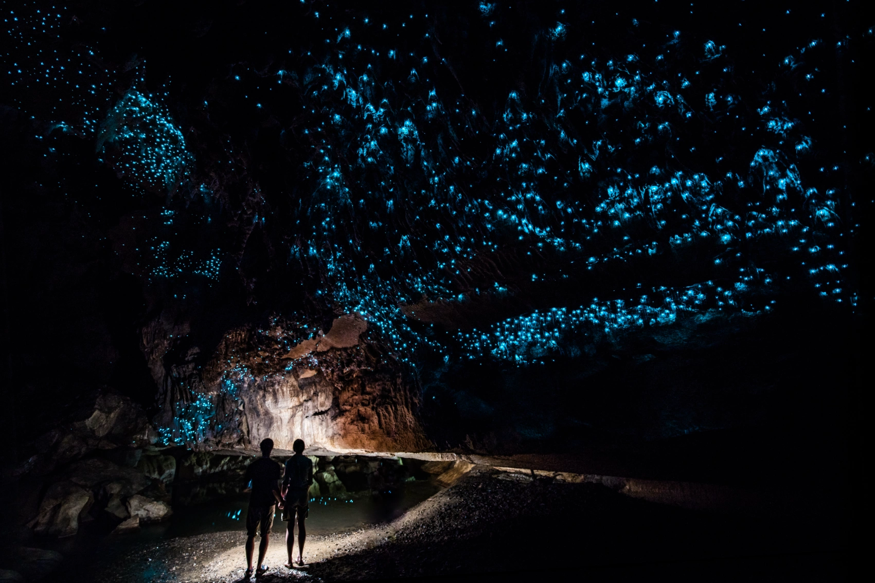 A couple stands below small glowing blue lights in New Zealand's glowworm caves