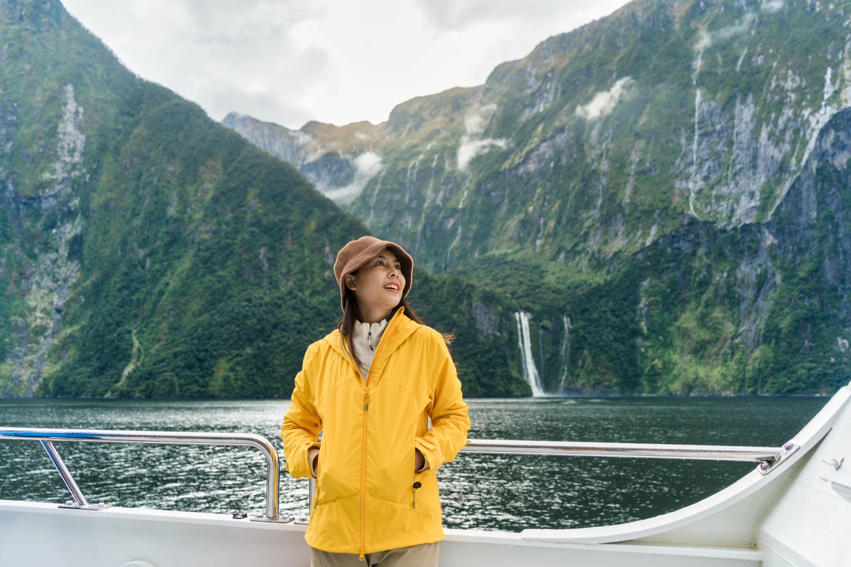 A woman traveller stands on a cruise boat in Milford Sound in New Zealand with mountains in the background