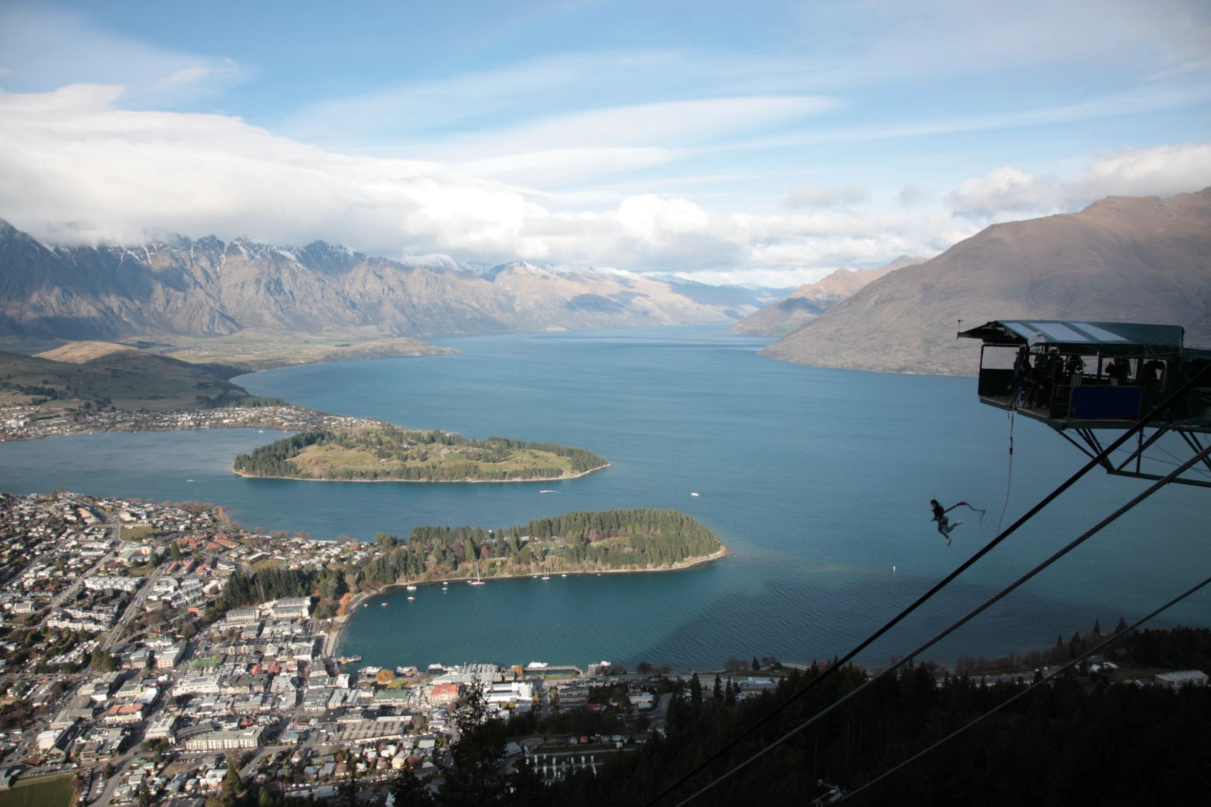 A silhouetted bungee jumper leaps from a platform with a view of Queenstown, New Zealand