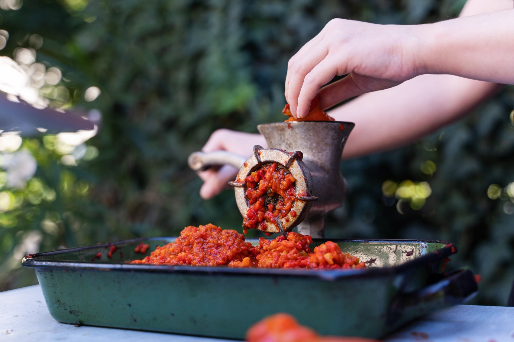 A person grinds red peppers into a dish to make pindjur in North Macedonia