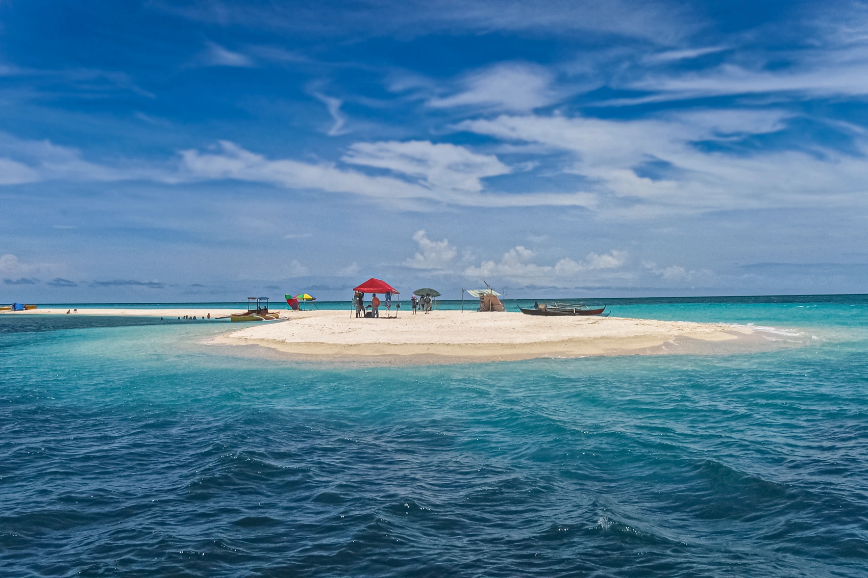 People set up umbrellas on a small patch of white sand surrounded by blue waters in the Philippines