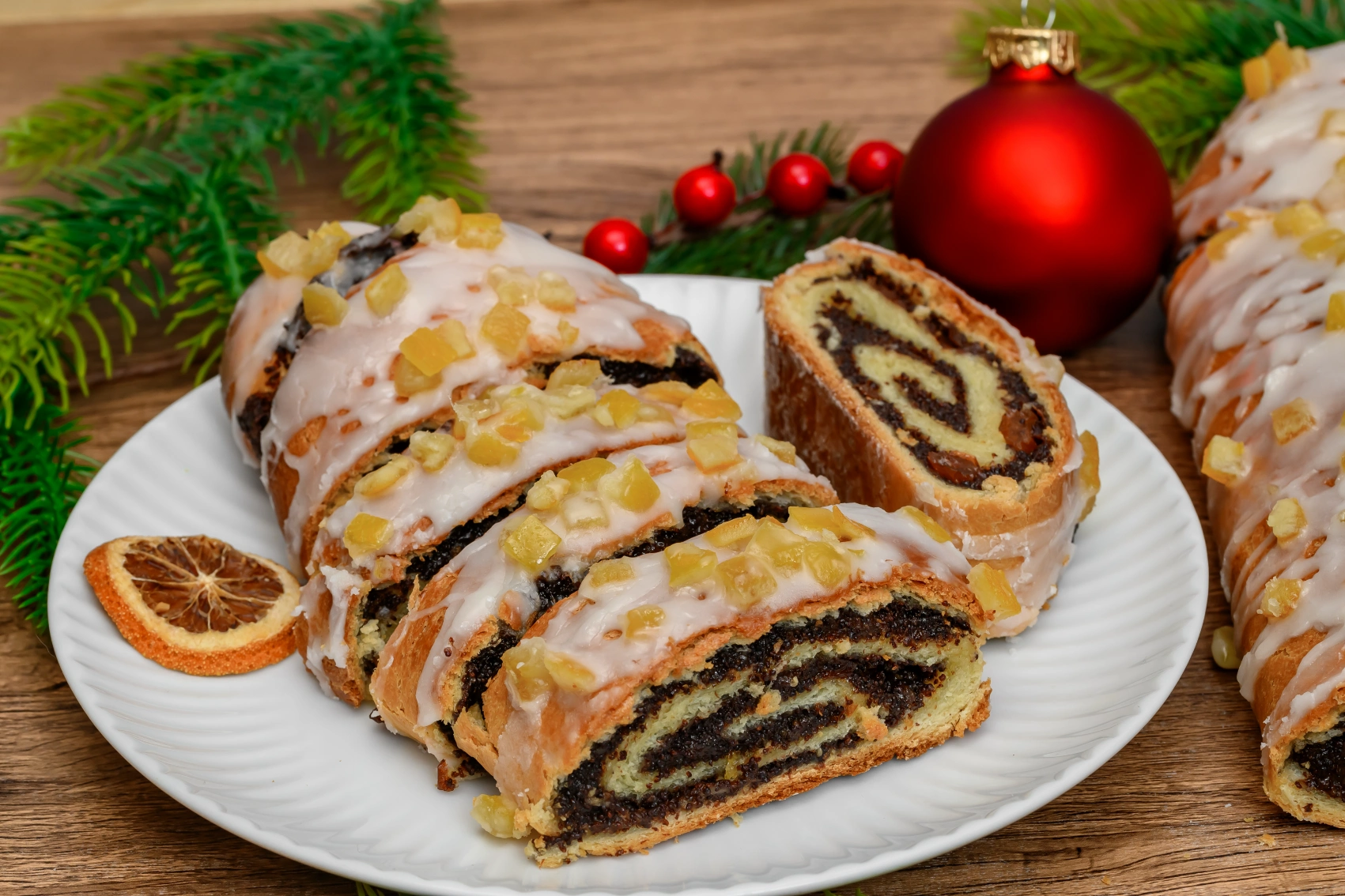 A sliced makowiec cake on a table surrounded by Christmas decorations in Poland