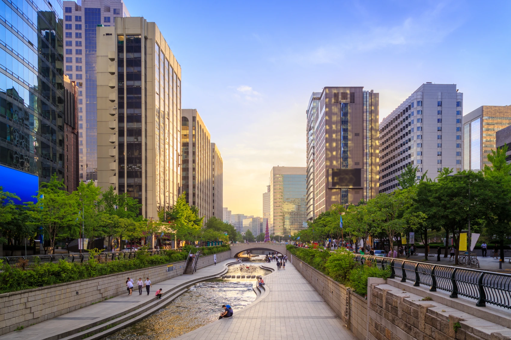 People walking and sitting by Cheonggyecheon Stream surrounded by modern buildings in Seoul, South Korea