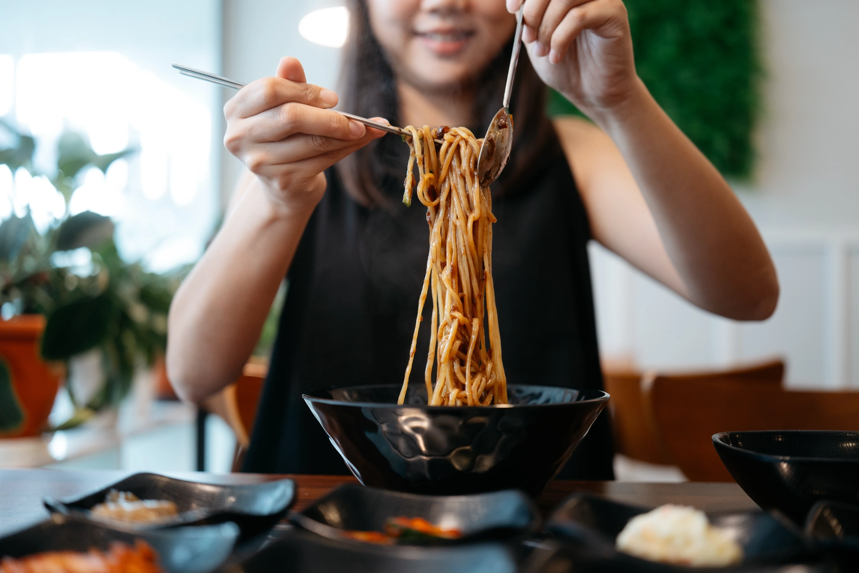 A woman traveller lifts jjajangmyeon noodles out of a bowl at a restaurant in South Korea