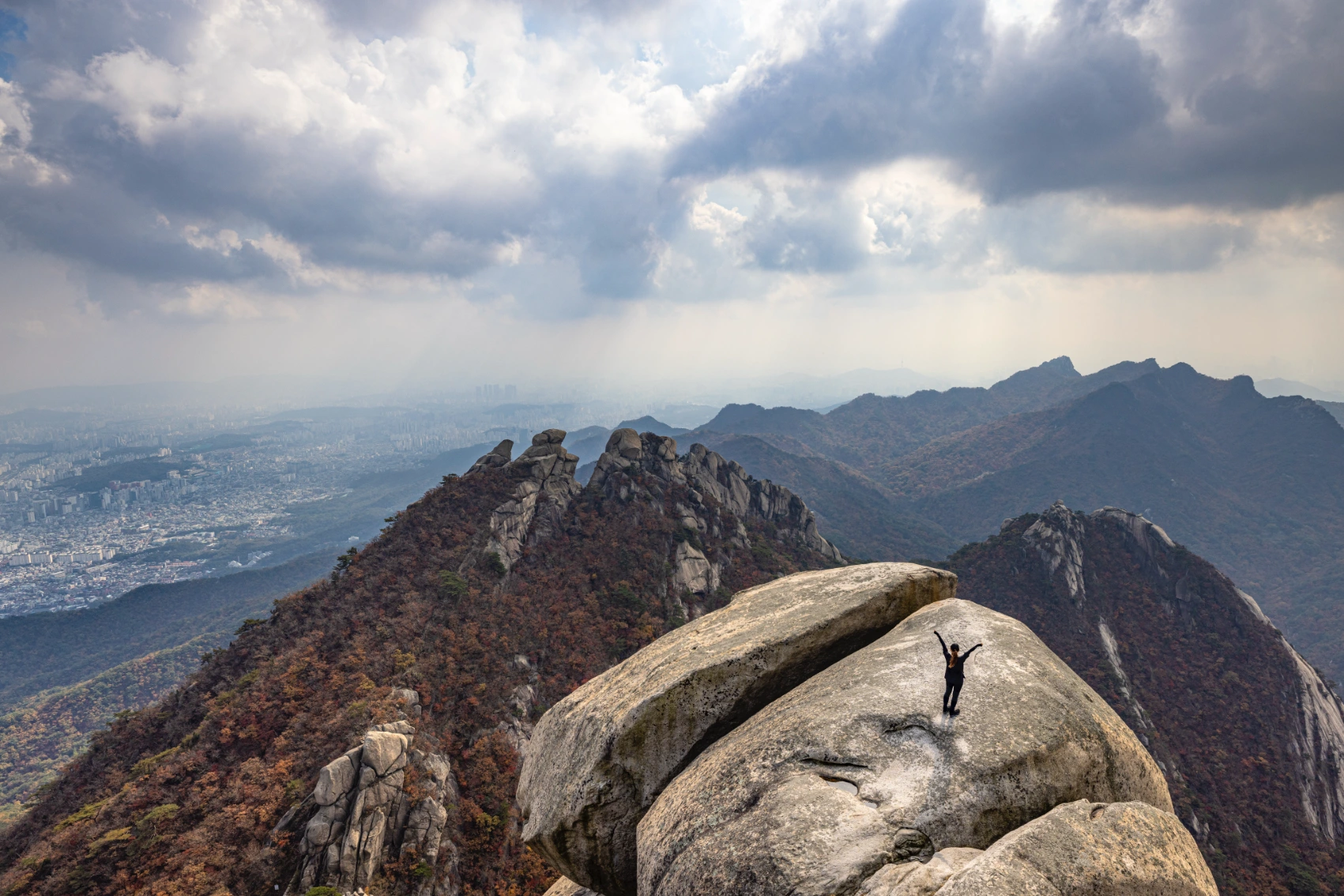 A hiker stands on a rocky outcrop with panoramic views in Bukhansan National Park, South Korea