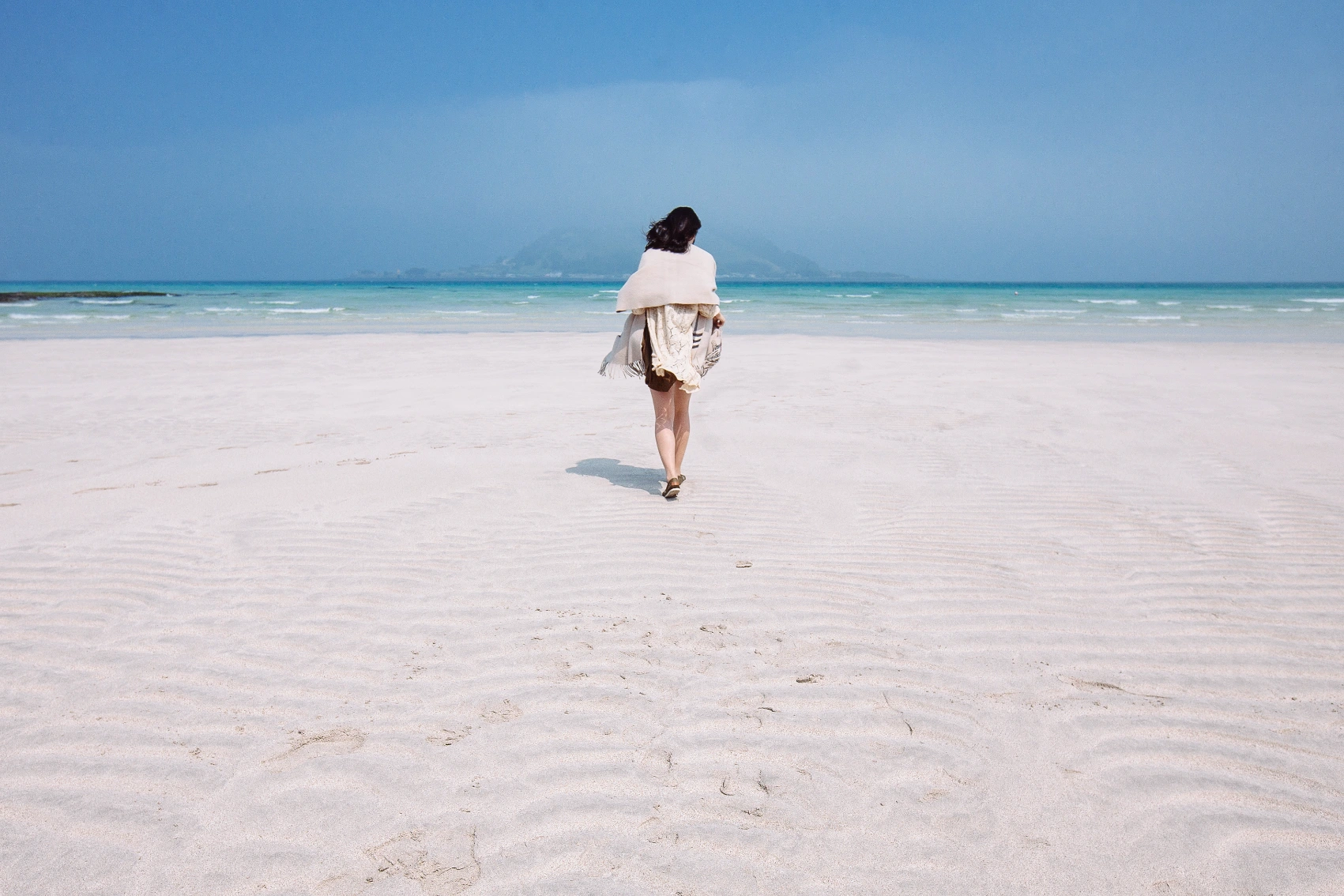 A woman traveller walks on a white-sand beach toward the ocean on Jeju Island in South Korea
