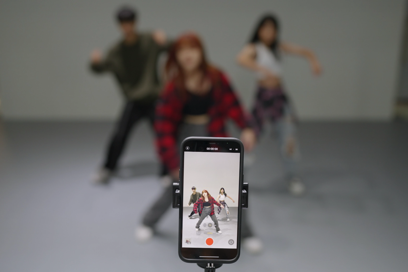 A group of friends dance in a studio while being recorded by a phone on a tripod in South Korea