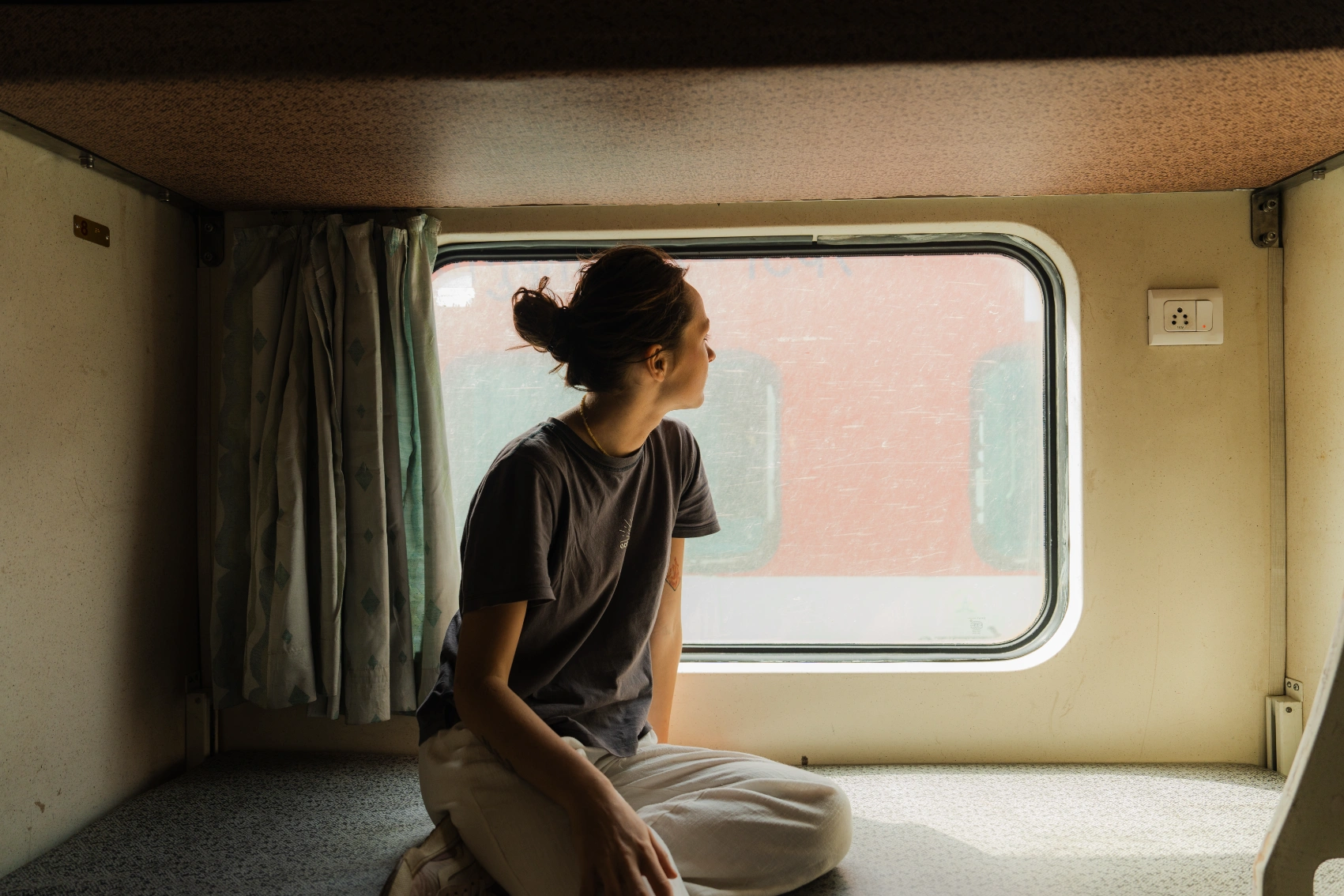 A woman traveller sits on a bed and looks out the window on a train in India