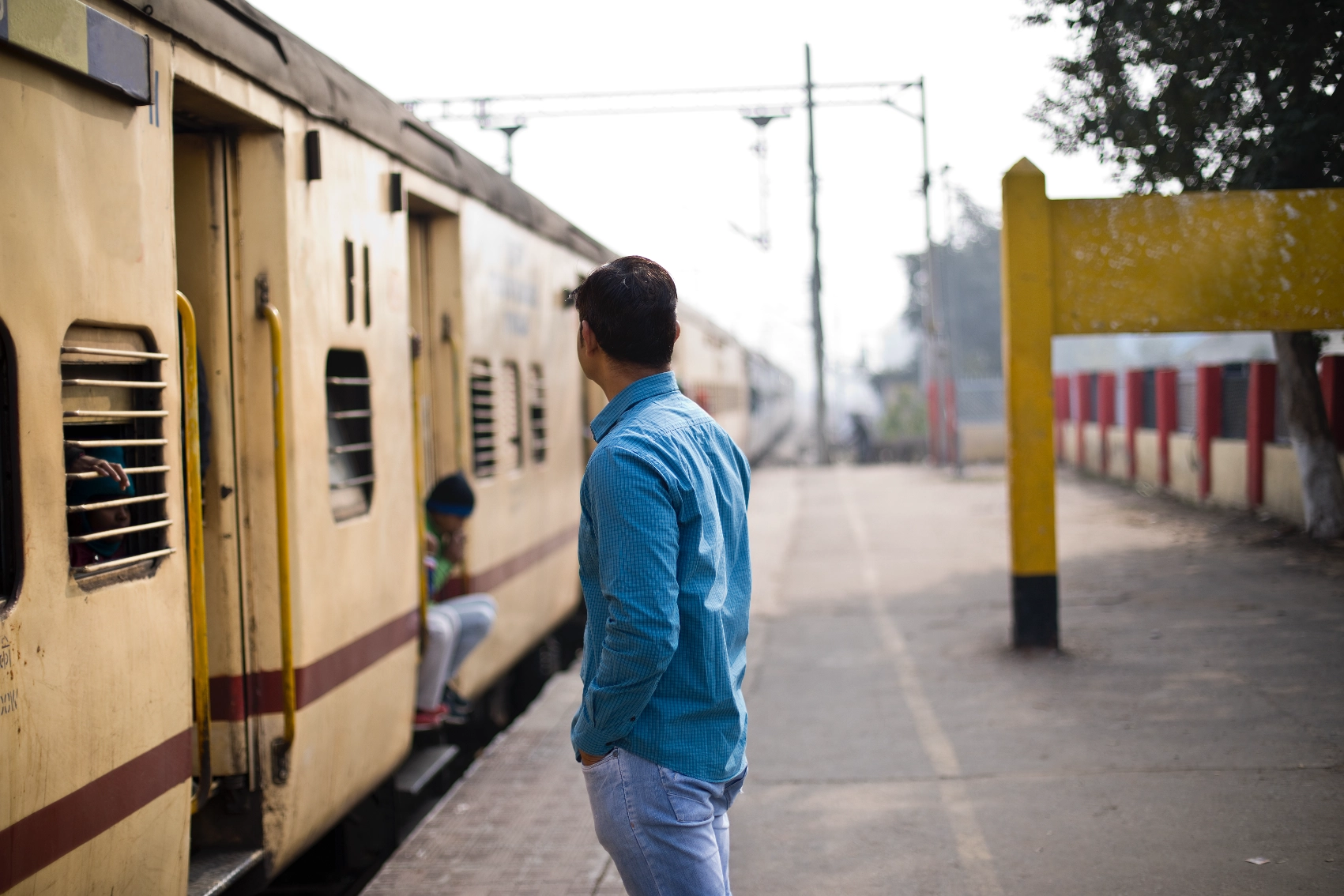 A man with his back to the camera waits on a train station platform in India
