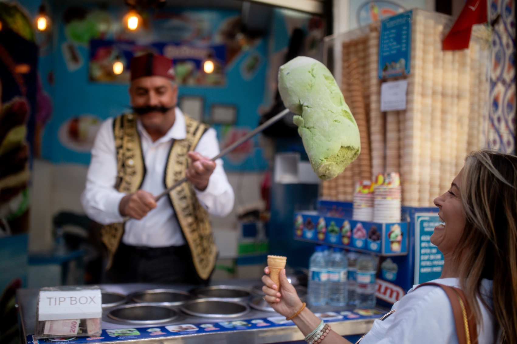A Turkish man holds out a large piece of dondurma ice cream while a traveller laughs in Istanbul