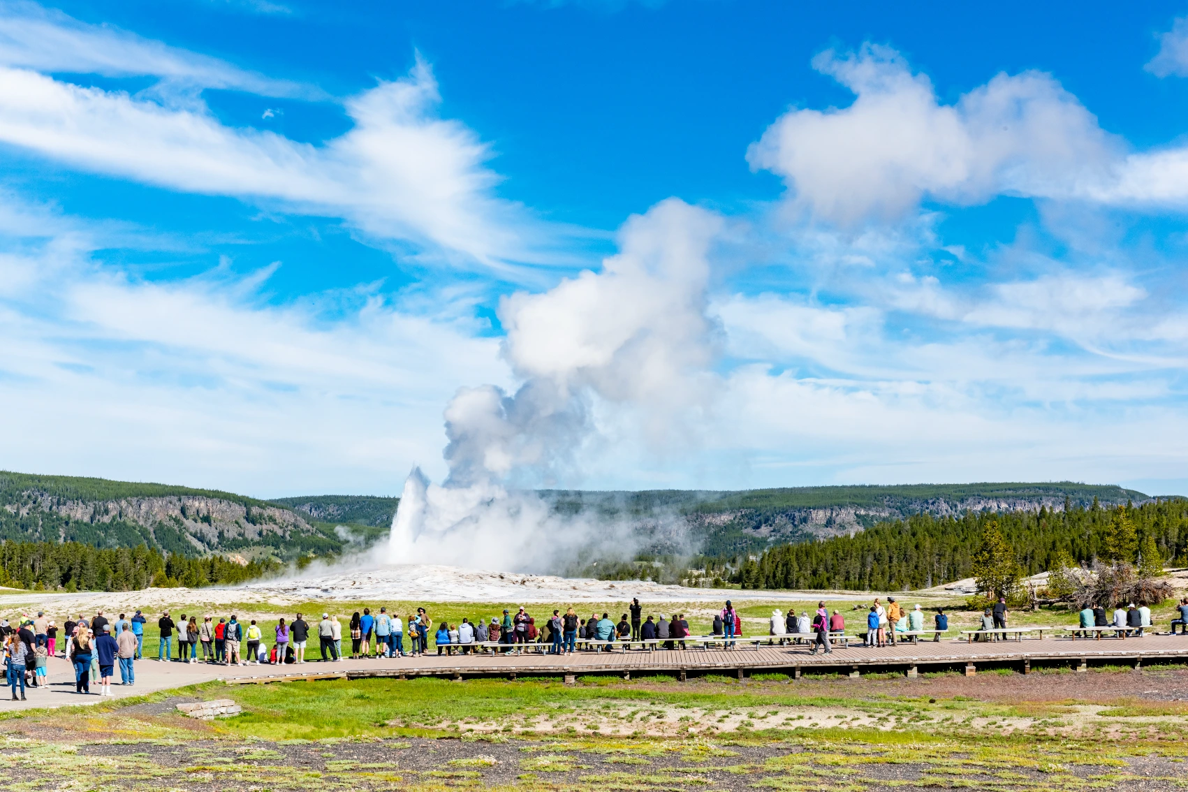 Old Faithful, Yellowstone National Park Travellers stand in front of a smoking geyser at Yellowstone National Park in Wyoming