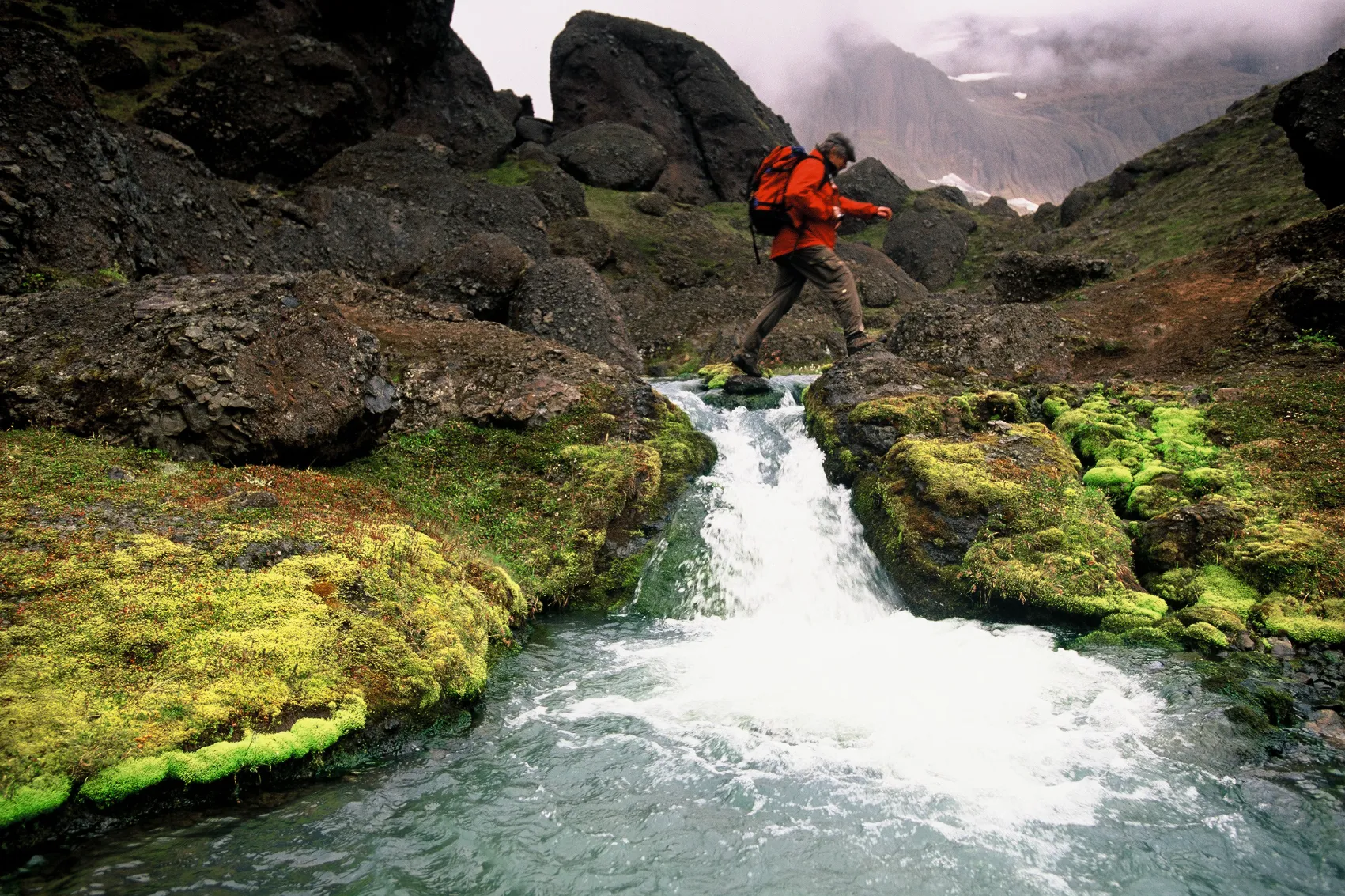 Hiking in Iceland A hiker crosses a small stream while trekking in Iceland