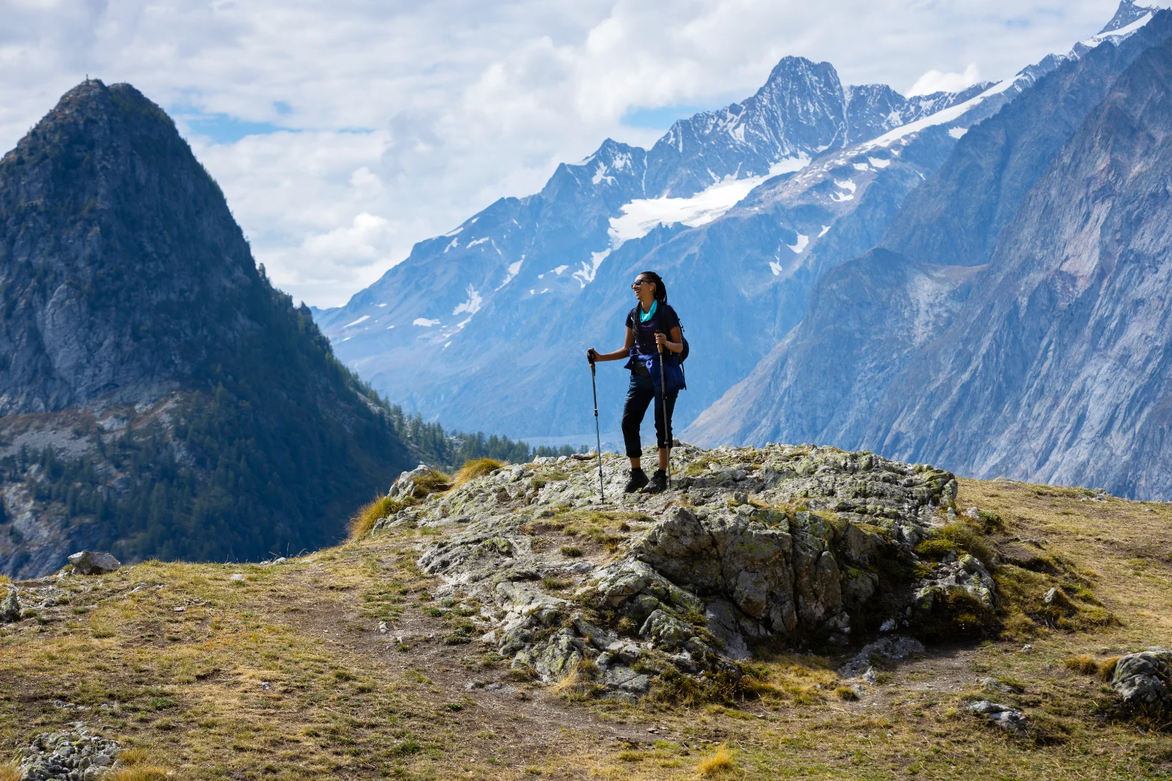 Hiking Mont Blanc A woman trekker stands on a rock while with a mountainous landscape in the background while hiking Mont Blanc