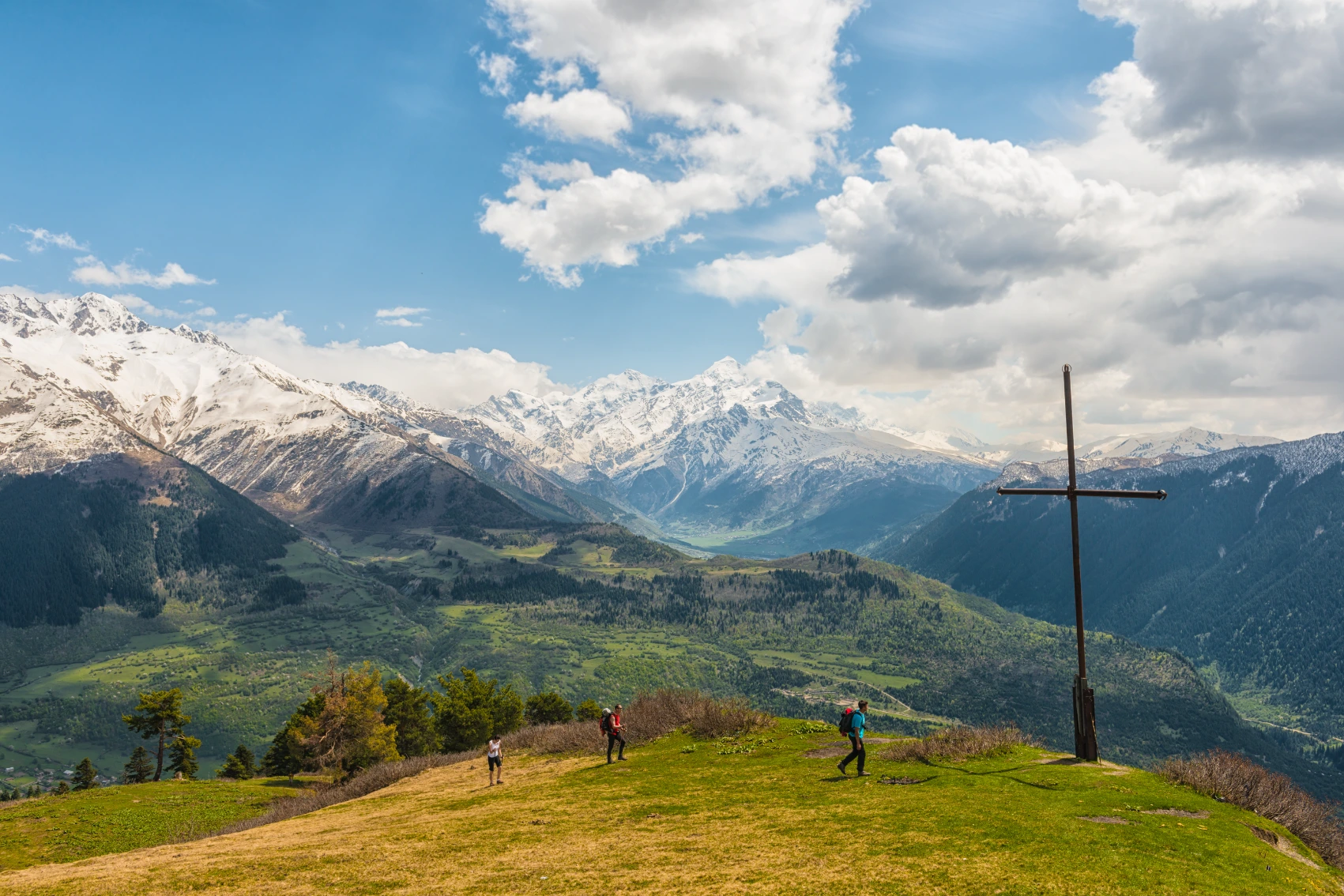 Mestia, Georgia Hikers walk near a large cross in the mountains of Mestia, Georgia