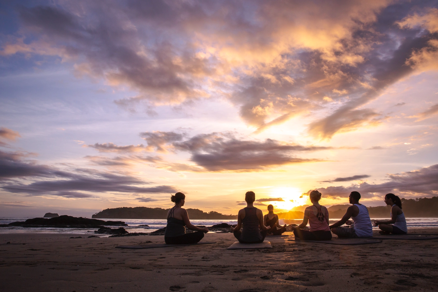 A group of travellers sit on the beach to meditate in Costa Rica