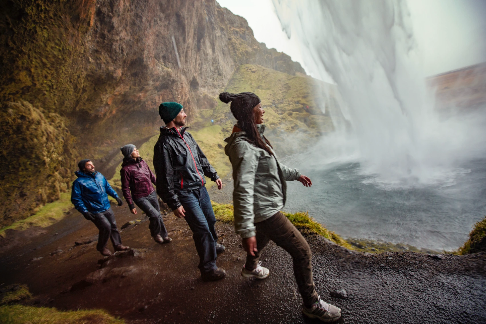 A group of travellers walks under a waterfall in Iceland