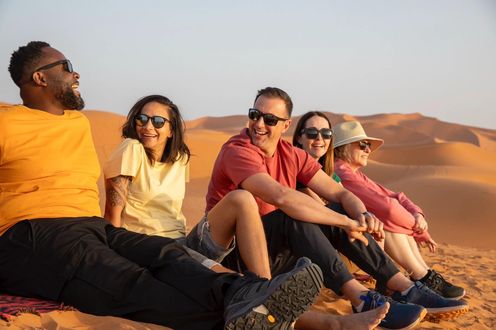 A group of travellers sits on a golden dune in Morocco