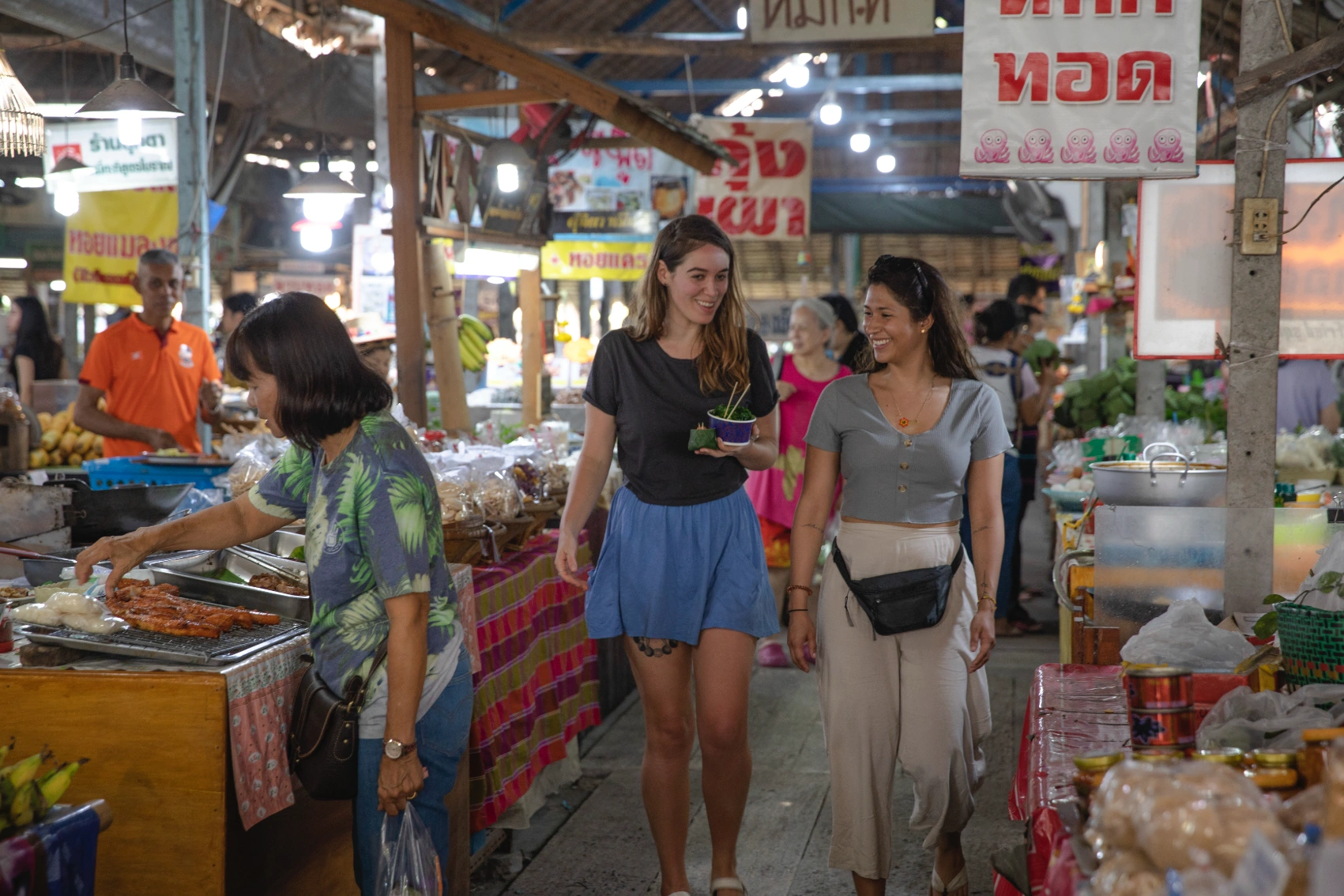 Two women travellers walk through a market in Thailand
