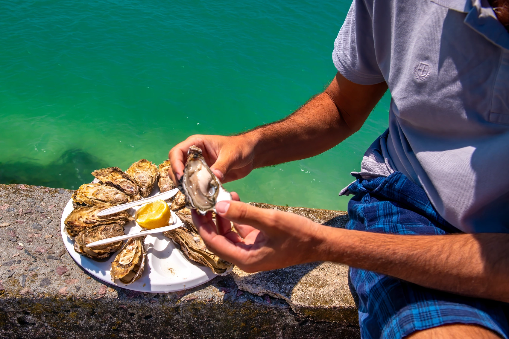 Normandy, France A traveller sits on a wall next to the sea to eat a tray of fresh oysters in Normandy, France