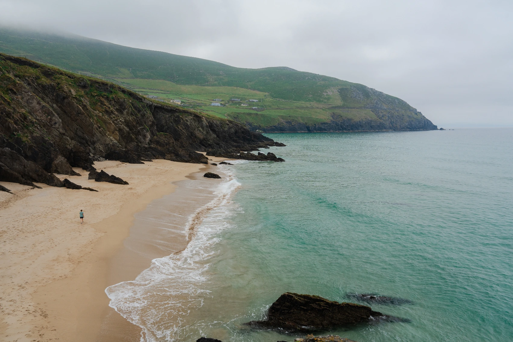 A man walks on a beach on the Dingle Peninsula on a cloudy day in Ireland