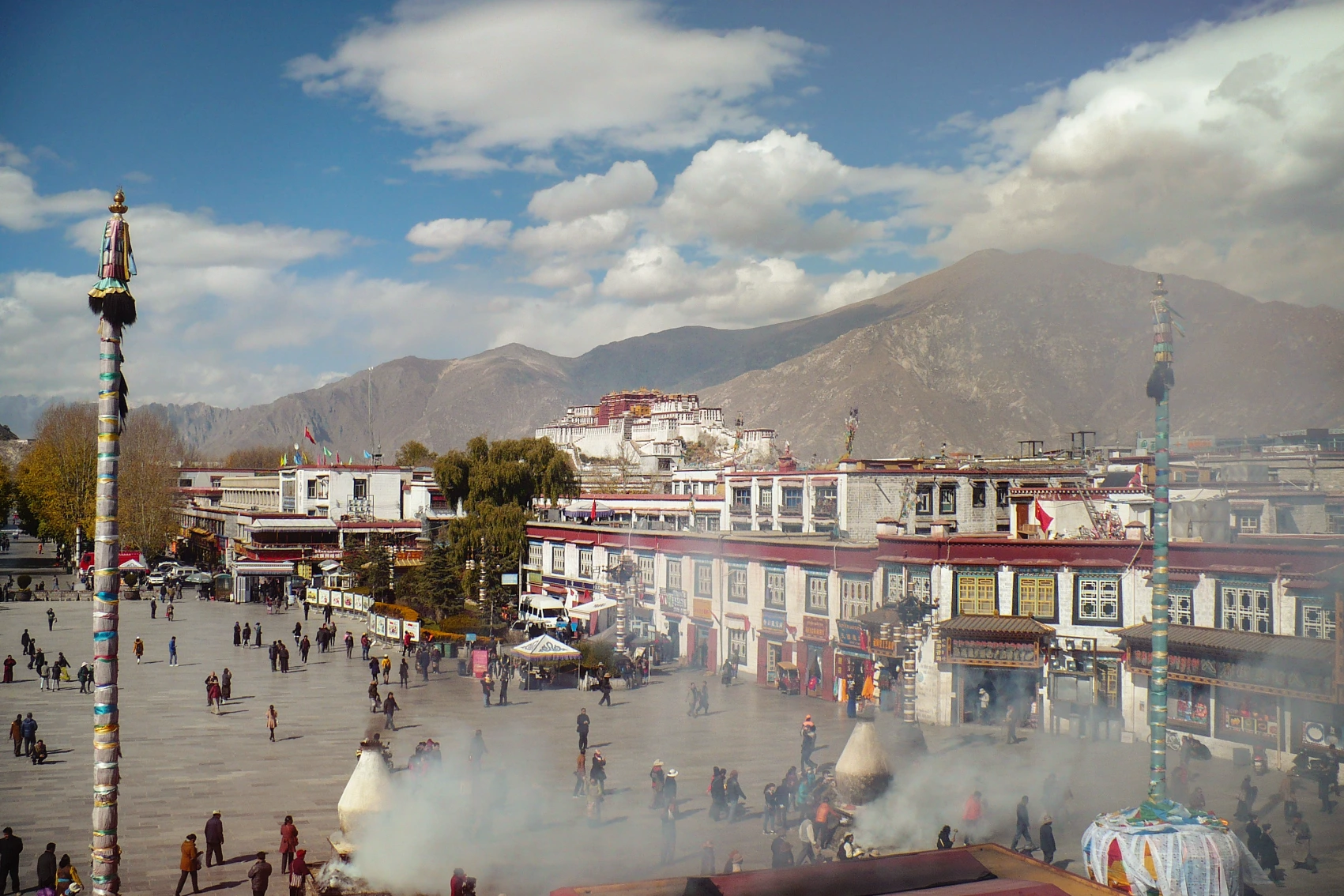 People walk around Jokhang Temple in Lhasa, Tibet, on a sunny day with mountains in the background