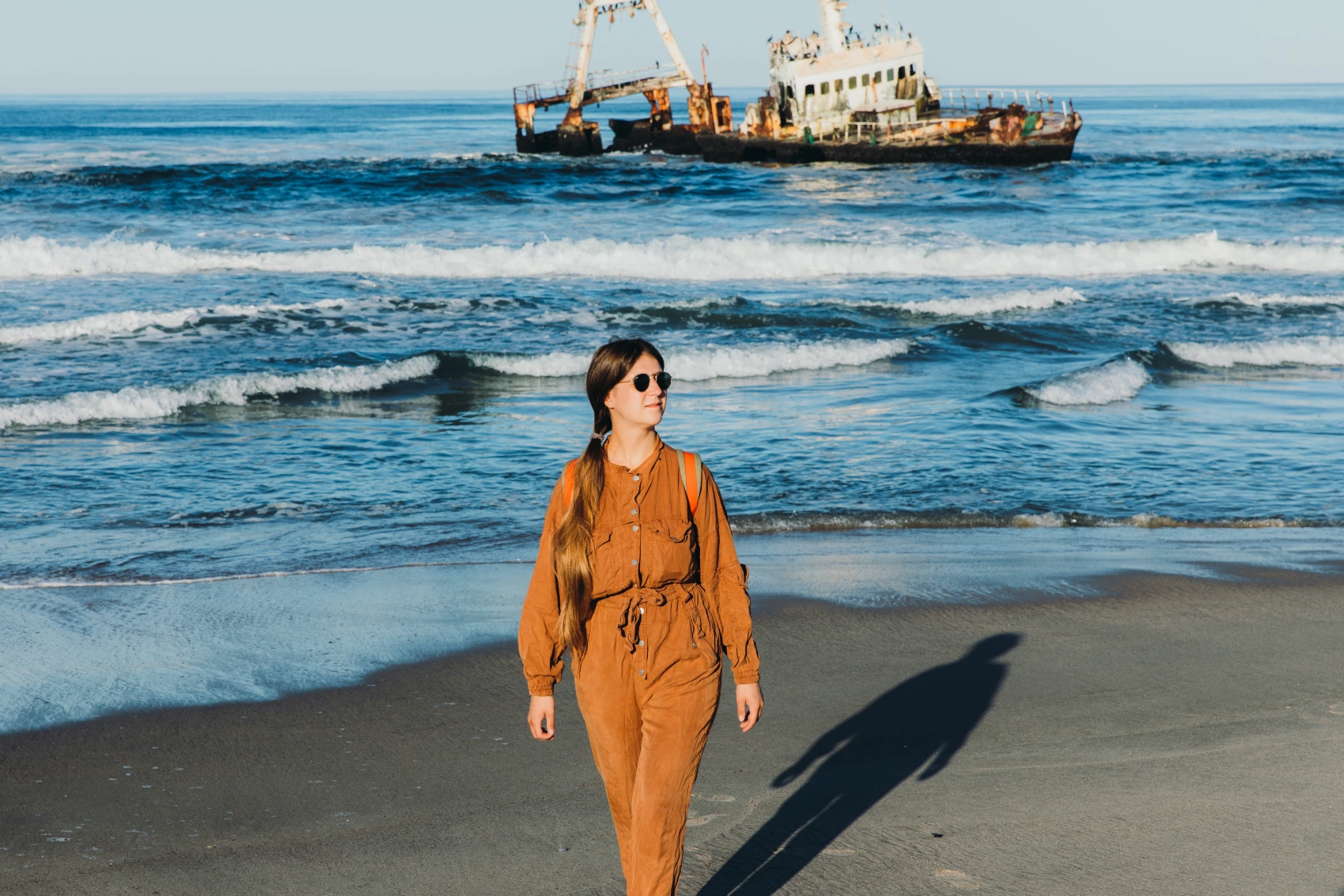 A woman traveller walks in front of a shipwreck on the Skeleton Coast, Namibia