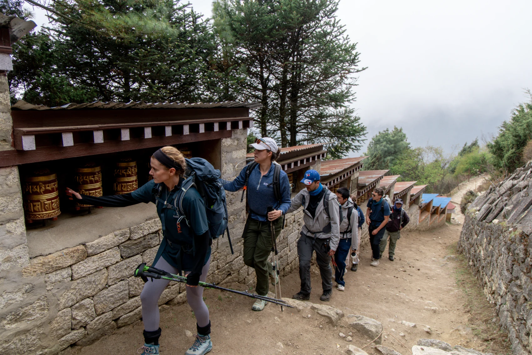 A group of hikers walks past prayer wheels in Nepal