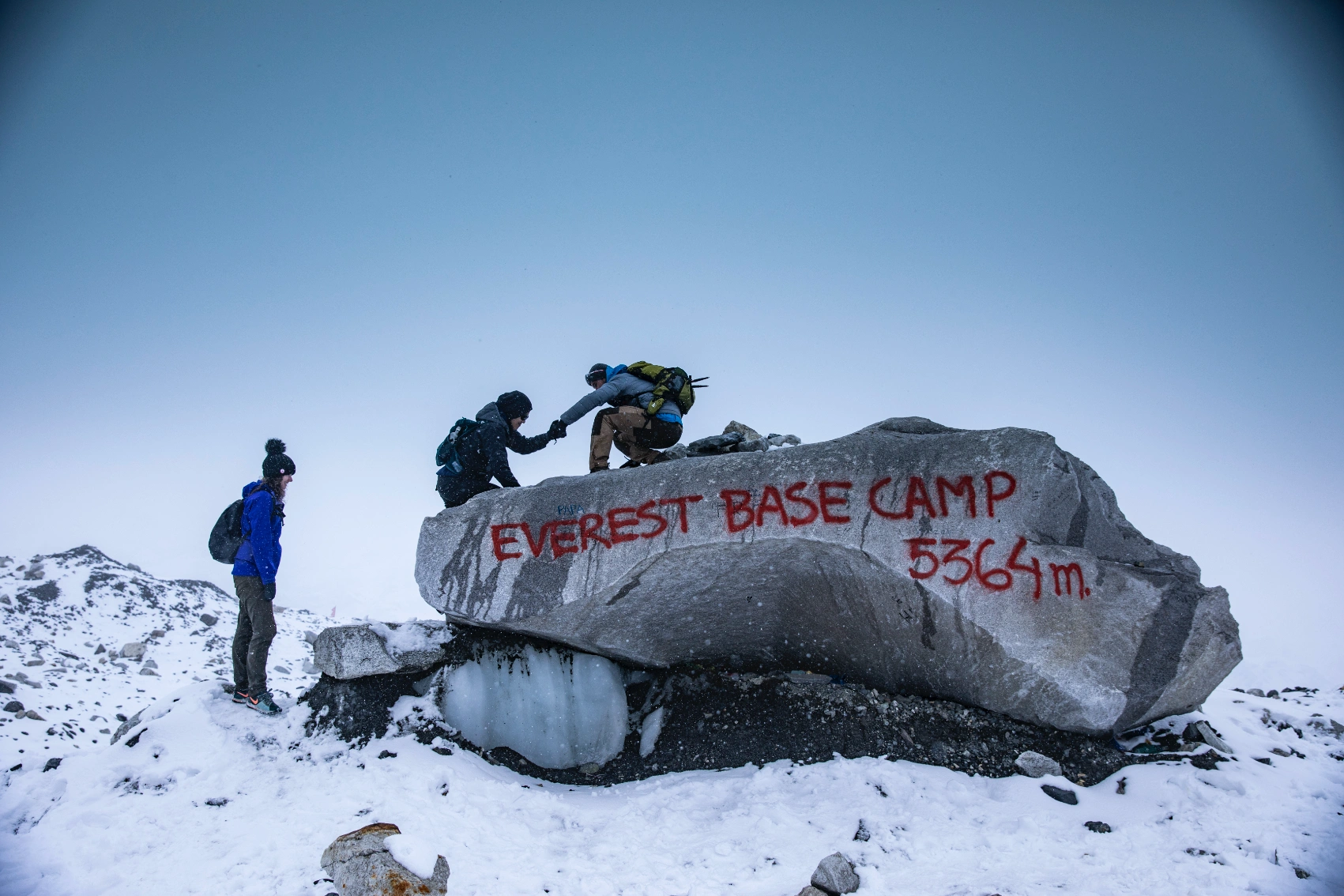 A group of trekkers climbs on a rock spray painted with Everest Base Camp in the snowy mountains of Nepal