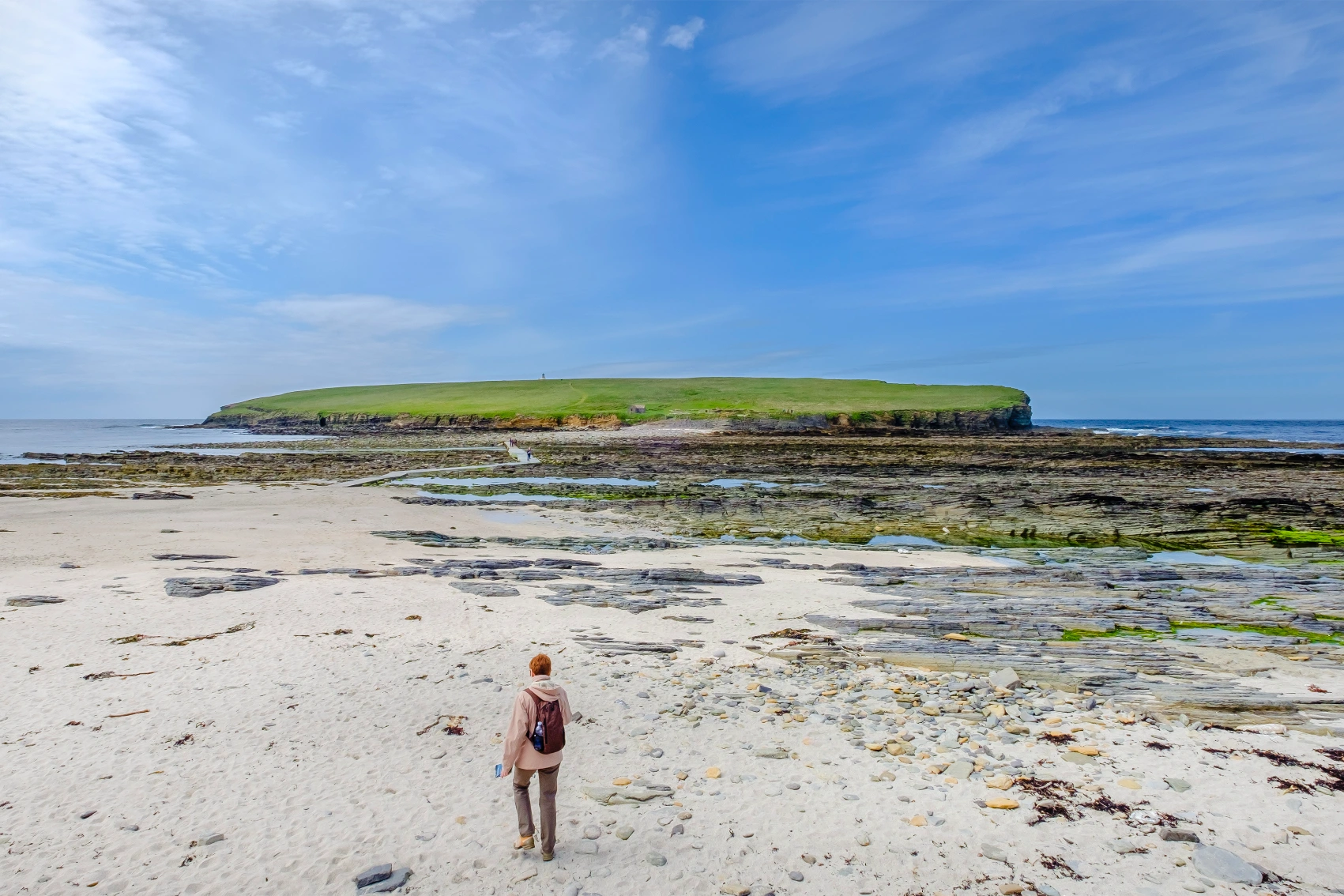 Orkney, Scotland A traveller walks on a sandy beach at low tide in Orkney, Scotland