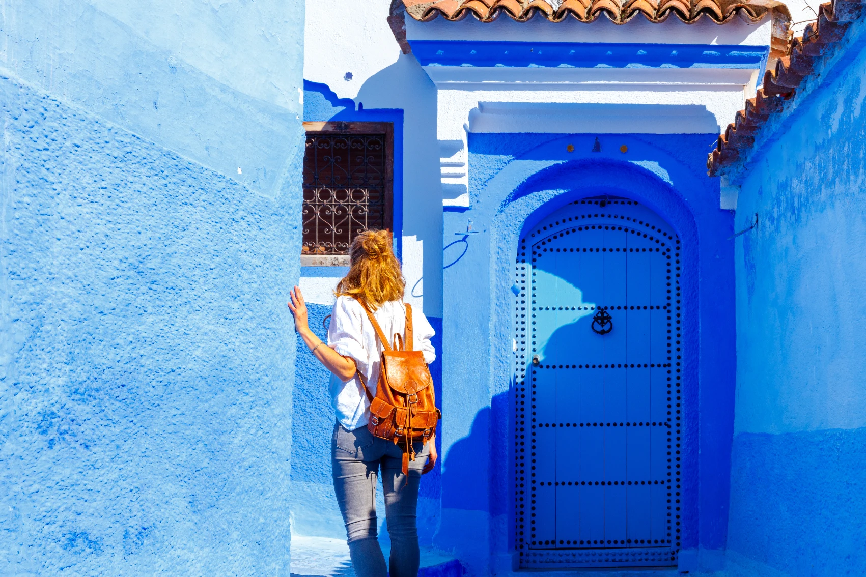 A woman traveller walks through a blue-painted alleyway in Chefchaouen, Morocco