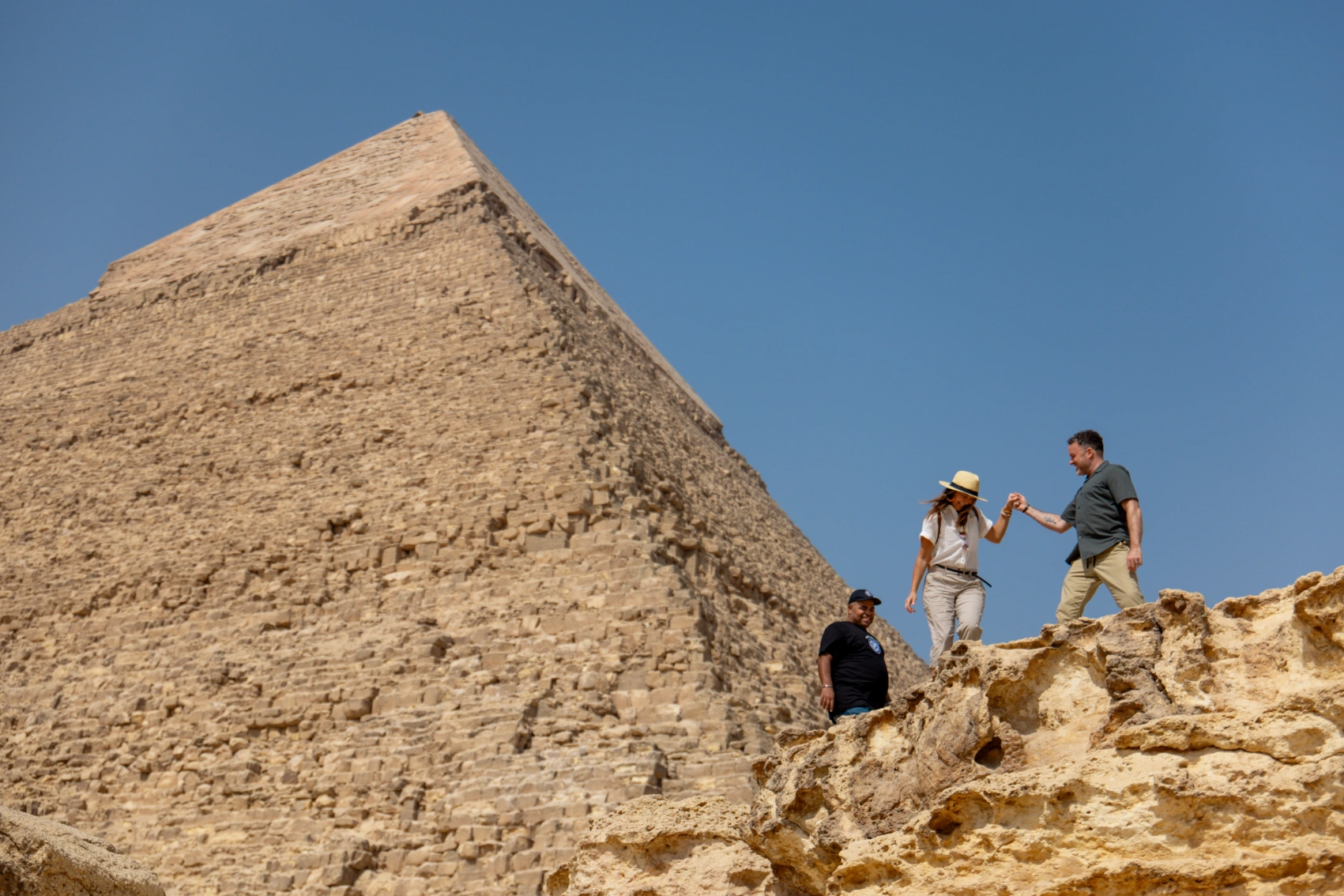 Travellers walk on stones with the Great Pyramid of Giza in the background