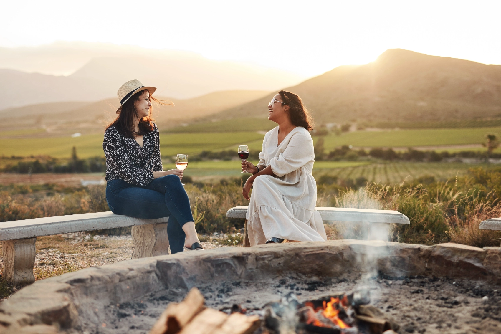 Two women travellers drink wine near a campfire