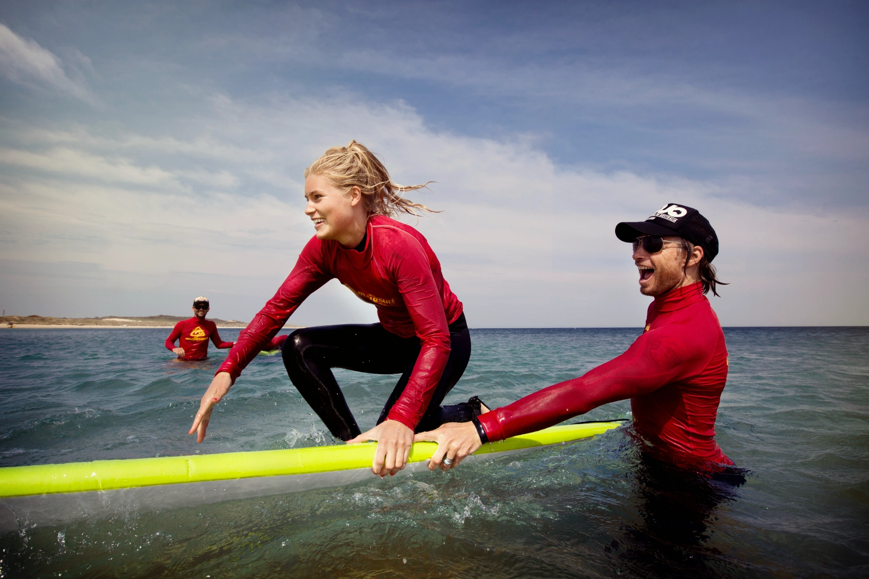 A woman starts to stand on a surfboard while being helped by an instructor in Australia