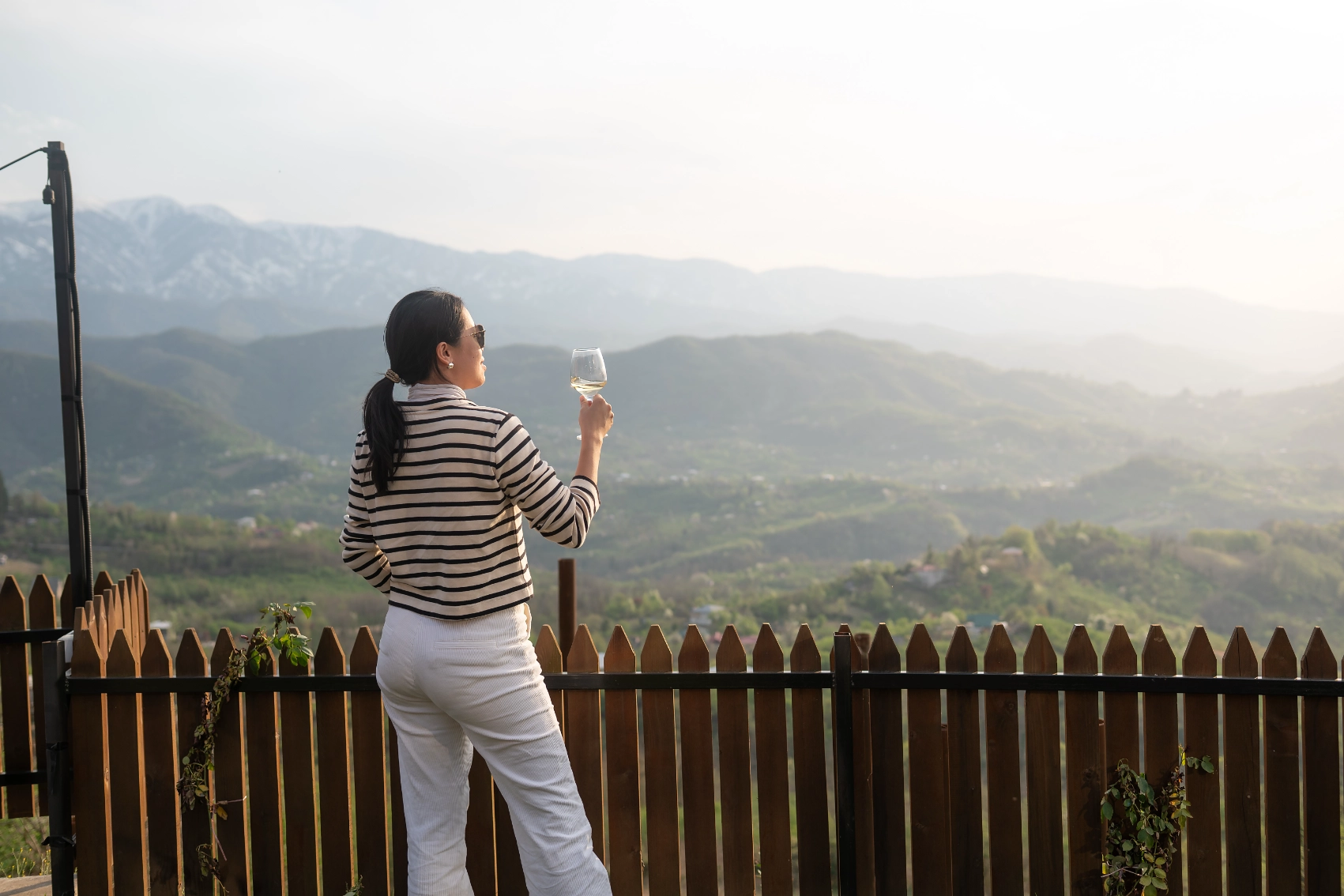 A woman traveller holds a glass of wine while looking out at the landscape of Georgia