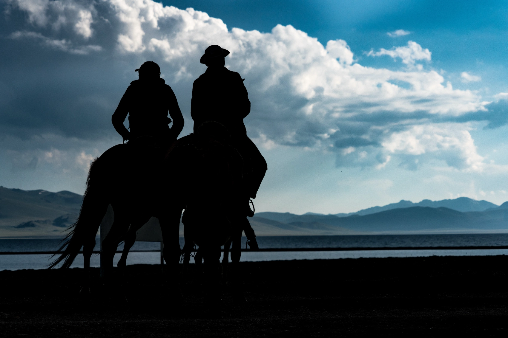 Two people on horseback in silhouette looking at a lake in Kyrgyzstan