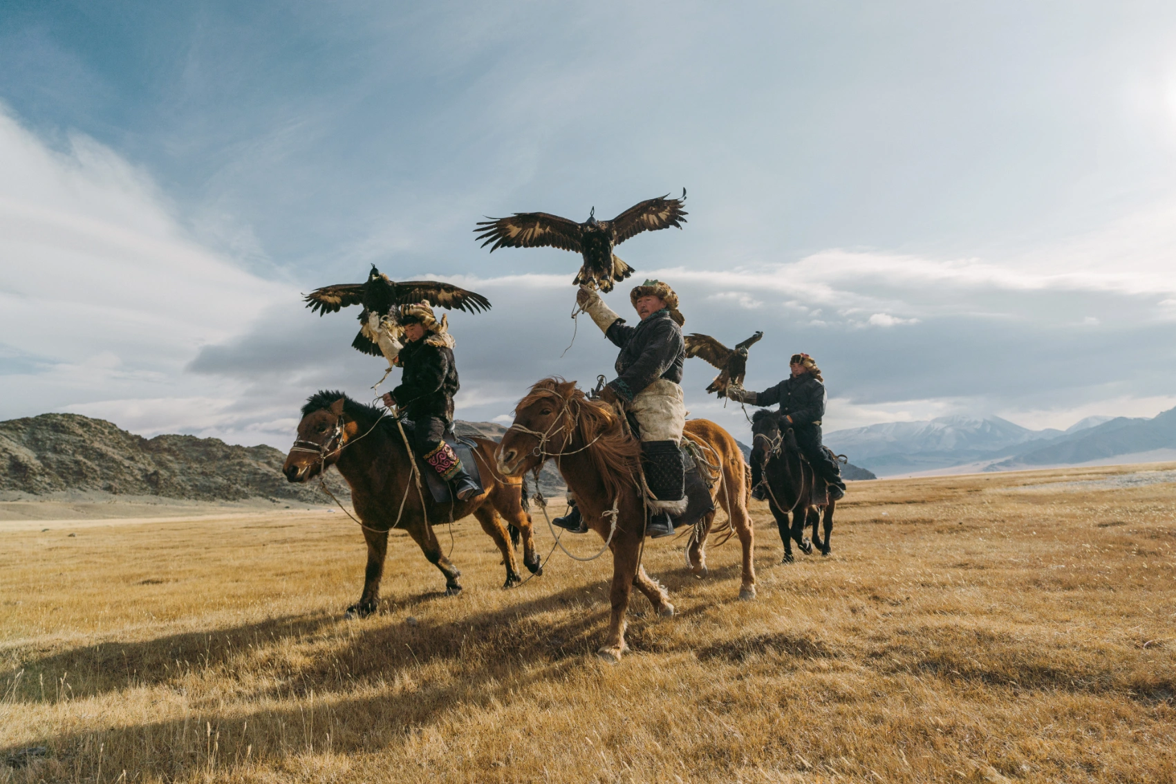 Three Mongolian riders on horseback hold up their hunting eagles