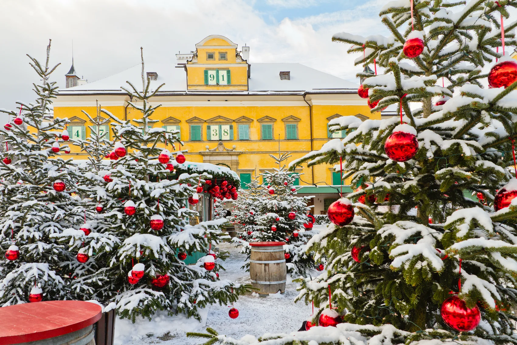Snow covers pine trees with red baubles at Hellbrunn Adventzauber in Salzburg, Austria