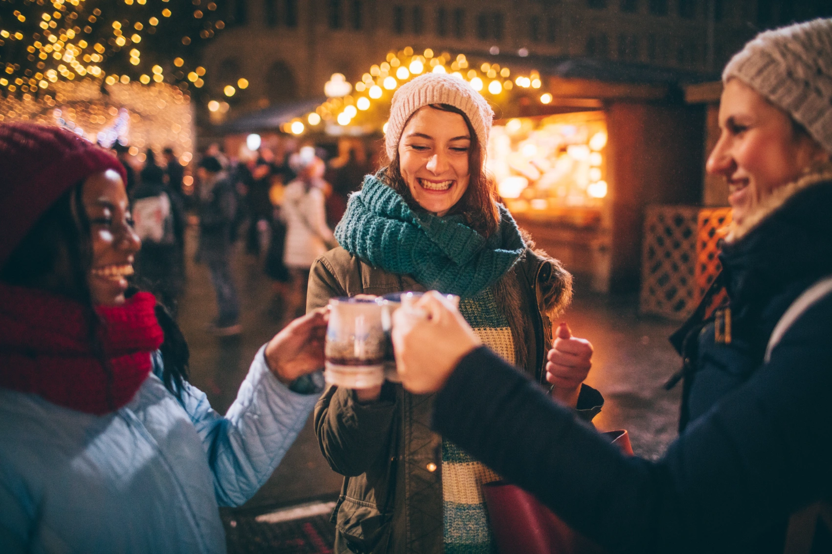 Three friends hold up mugs of mulled wine at the Christmas market in Vienna, Austria