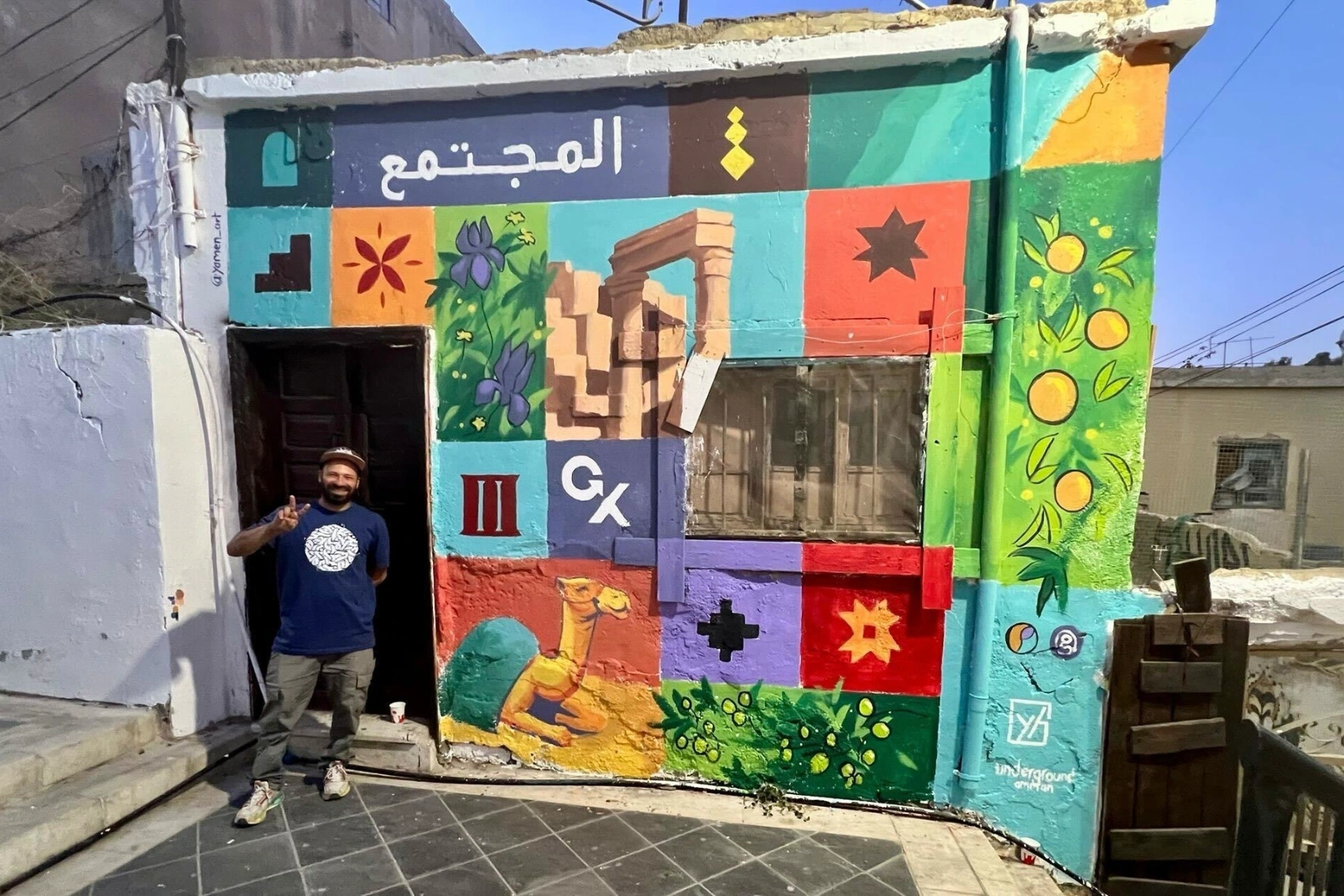A man stands in a shop door surrounded by a mural painted for World Tourism Day 2025 in Amman, Jordan