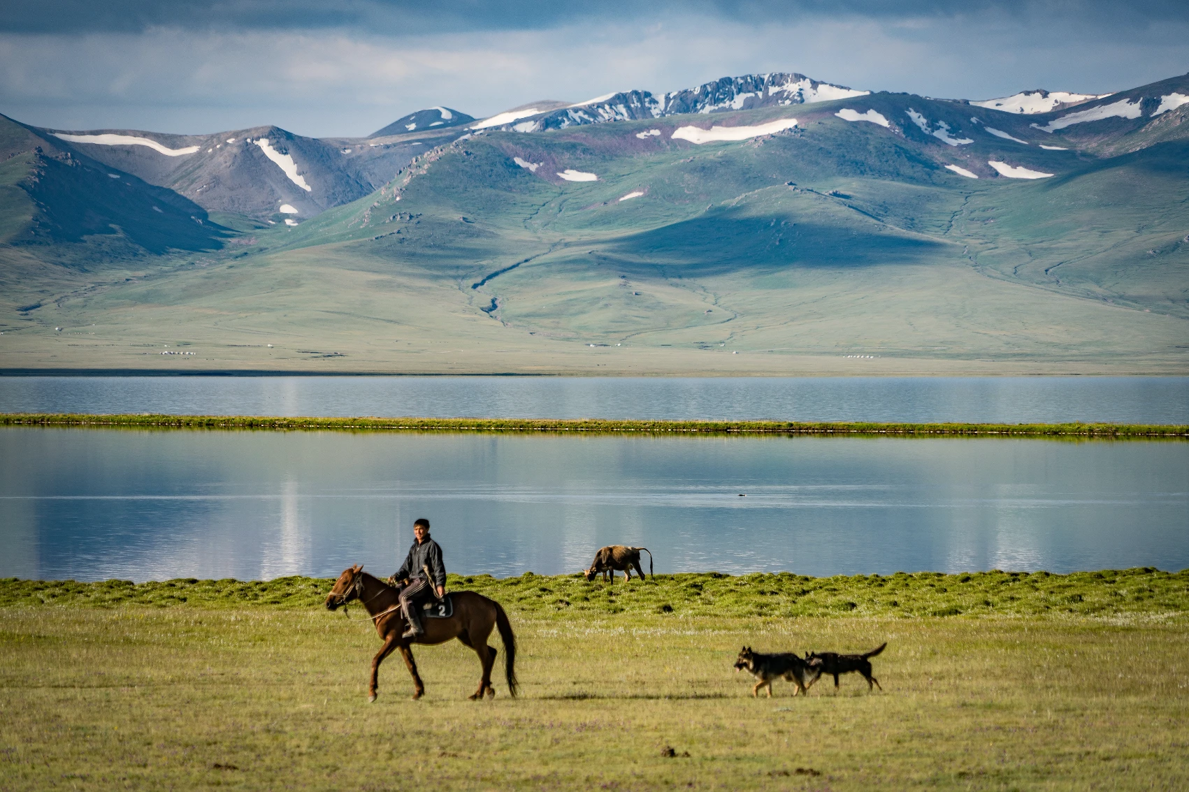 A man on a horse rides in front of a lake in Kyrgyzstan