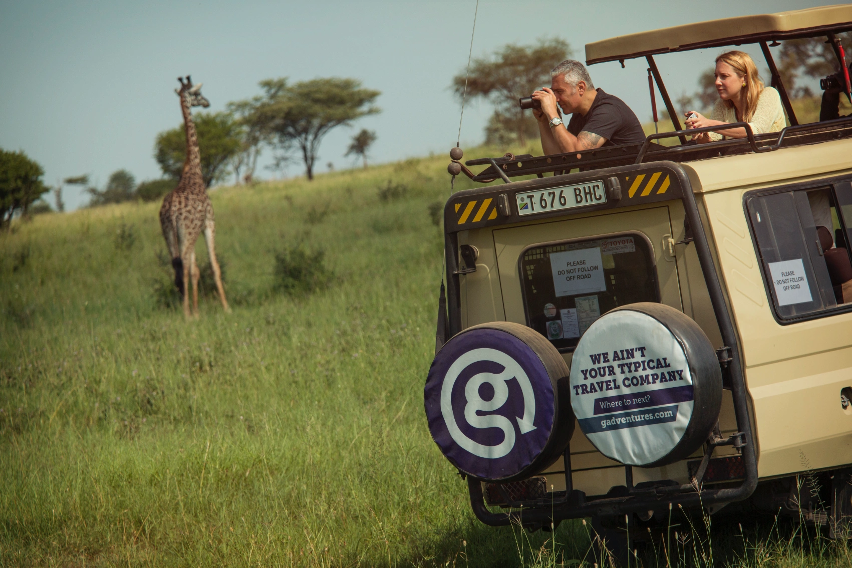 A man stands in a safari vehicle to take a photo of a giraffe in Southern Africa