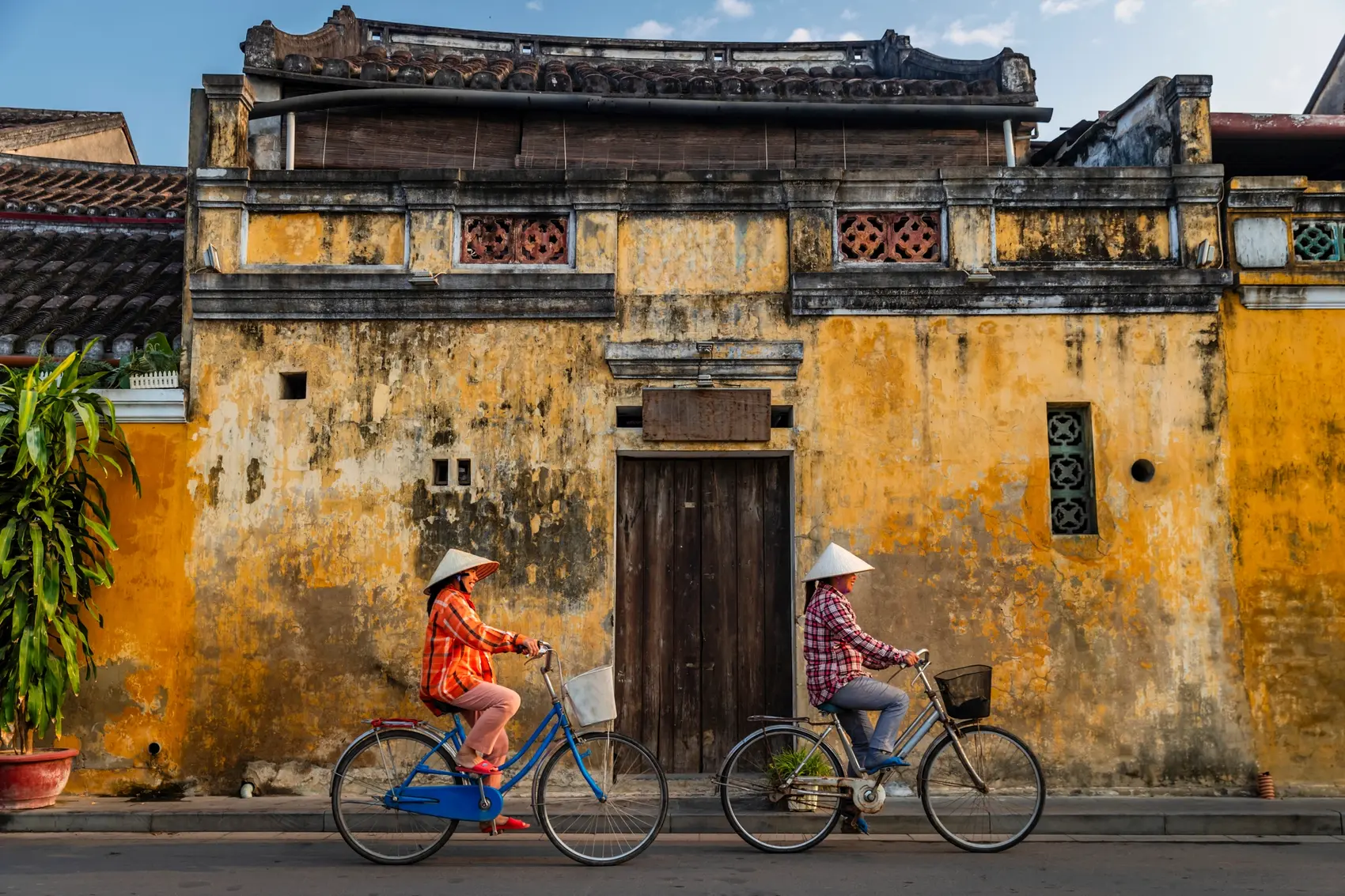 Two Vietnamese women ride bicycles in the old town of Hội An