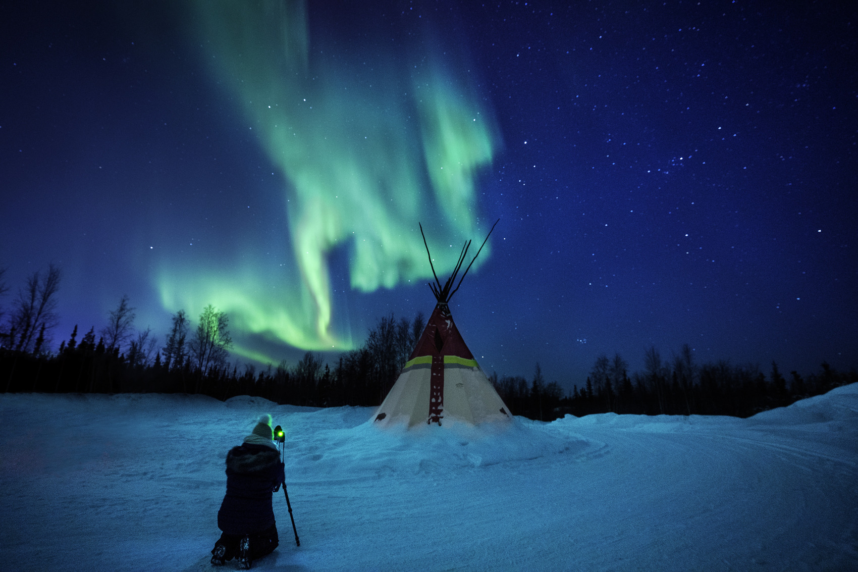 The Northern Lights flickering over a man by a teepee in Canada