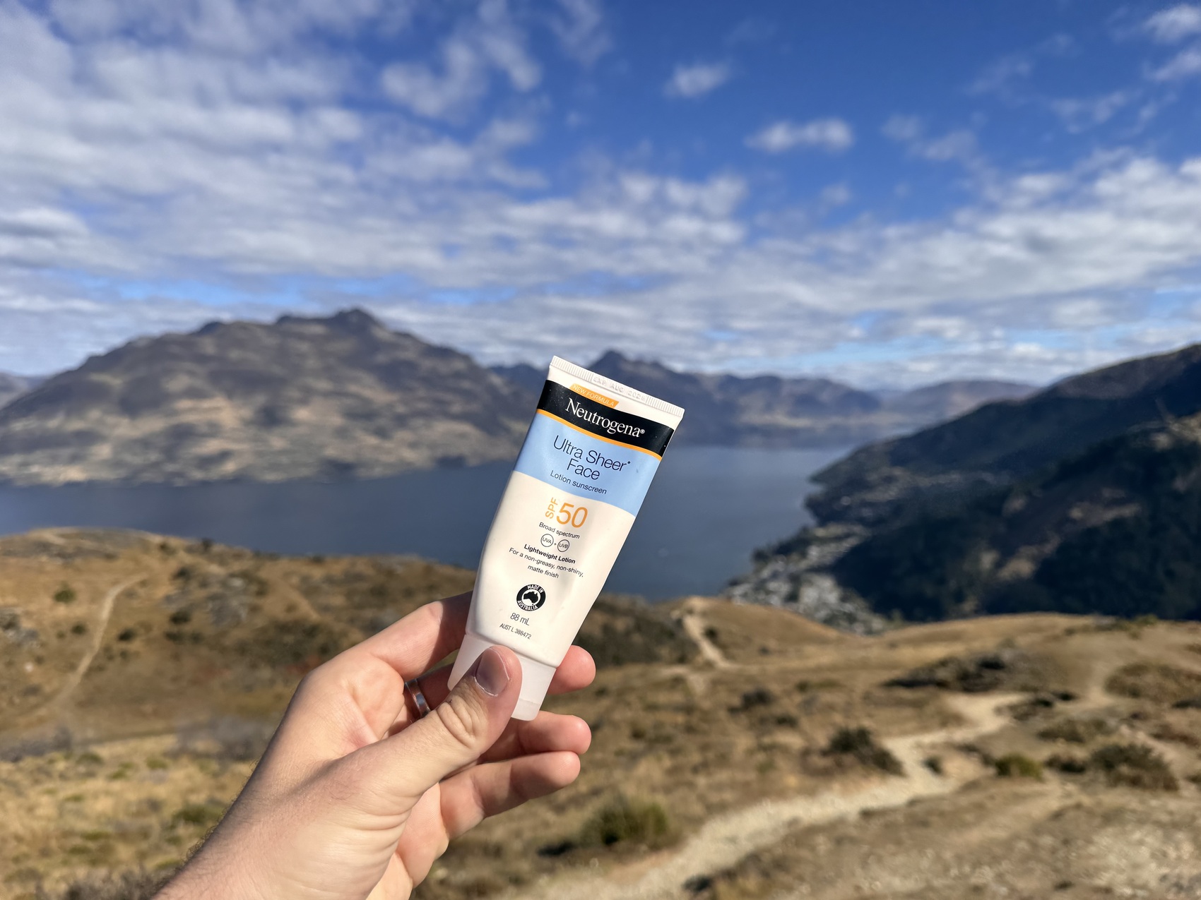 Someone holding up some sunscreen in front of a picturesque New Zealand backdrop