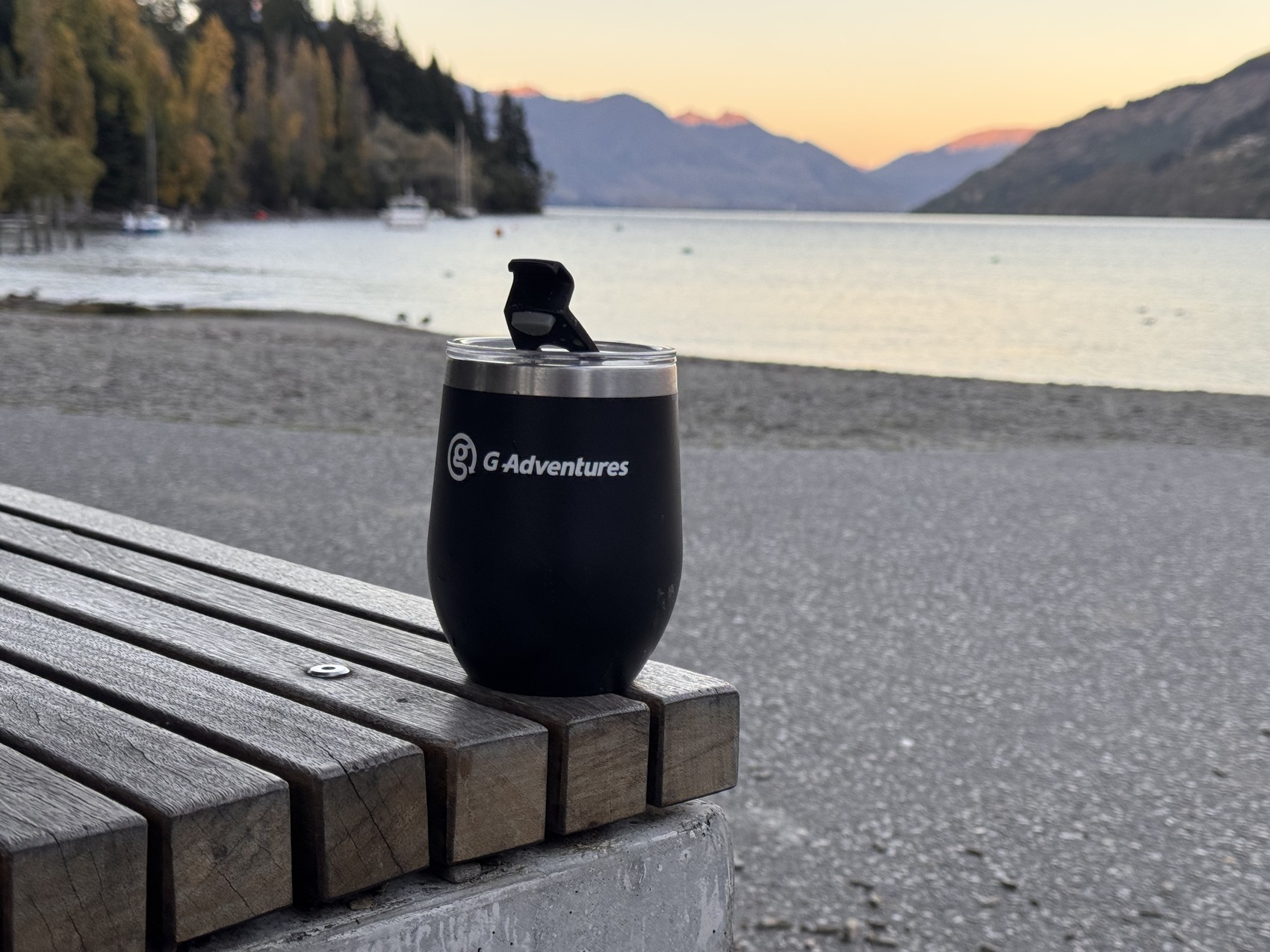 A G Adventures&rsquo; mug filled with a hot drink in front of a beautiful Kiwi sunset panorama